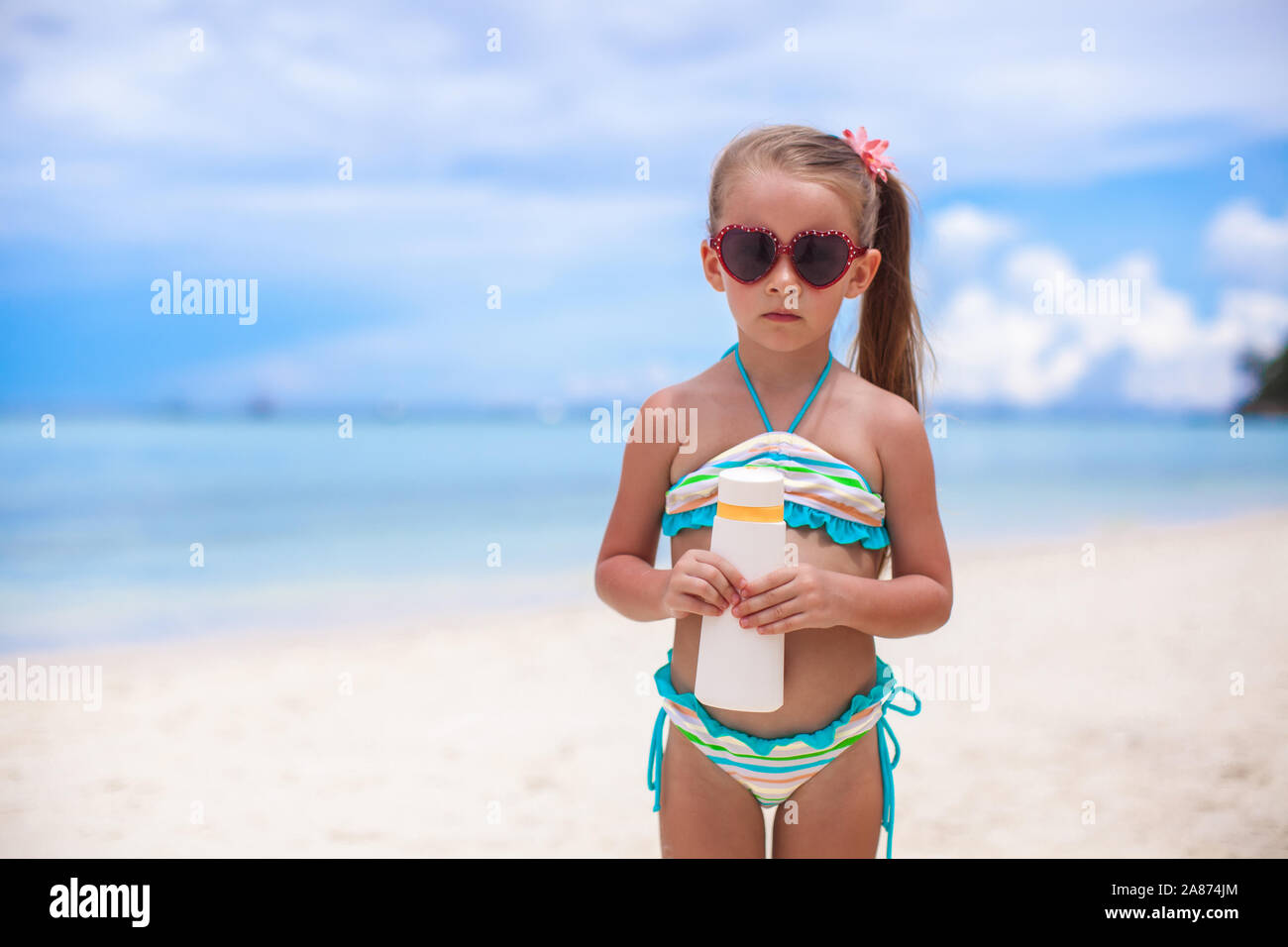 Peu jolie fille en maillot de bain est titulaire d'une lotion solaire bouteille Banque D'Images