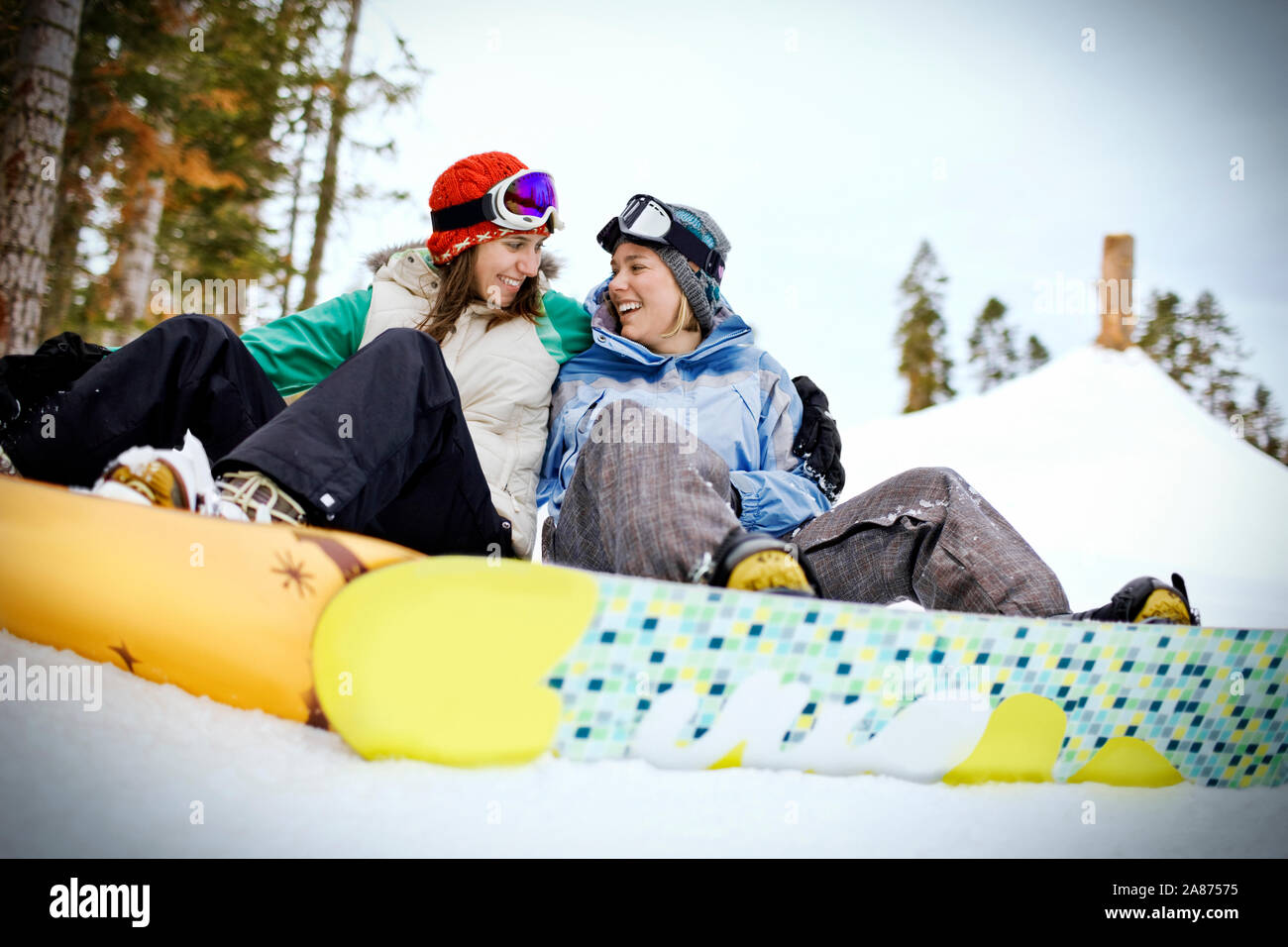 Deux jeunes femmes souriant assis à côté de l'autre tout en restant fixé à snowboards et assis dans la neige. Banque D'Images