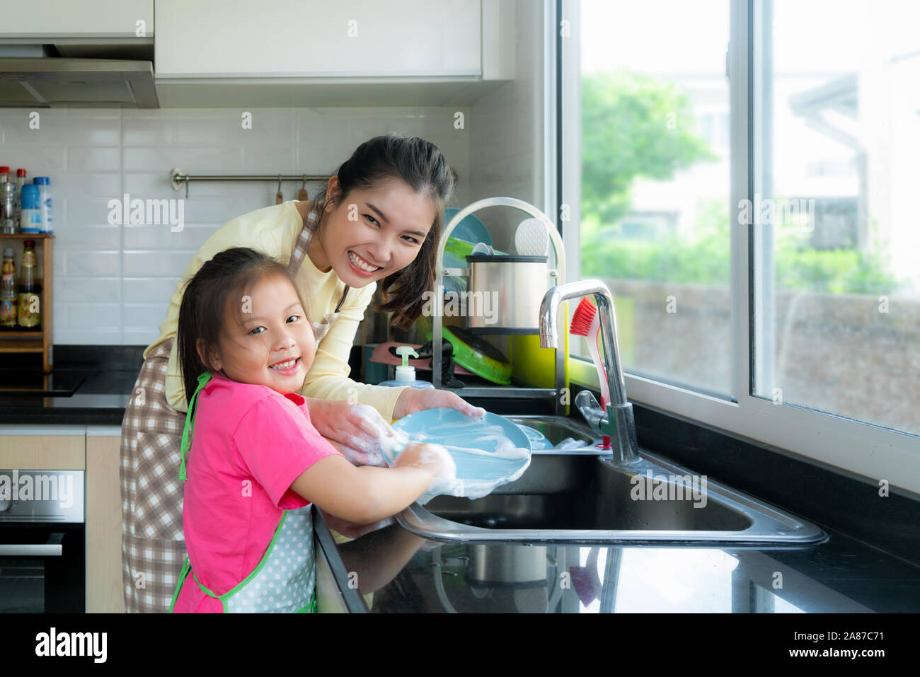 Belle asiatique de droits tout en lave-vaisselle ensemble avec du détergent sur l'évier dans la cuisine à la maison. Famille heureuse temps à l'enseignement Banque D'Images