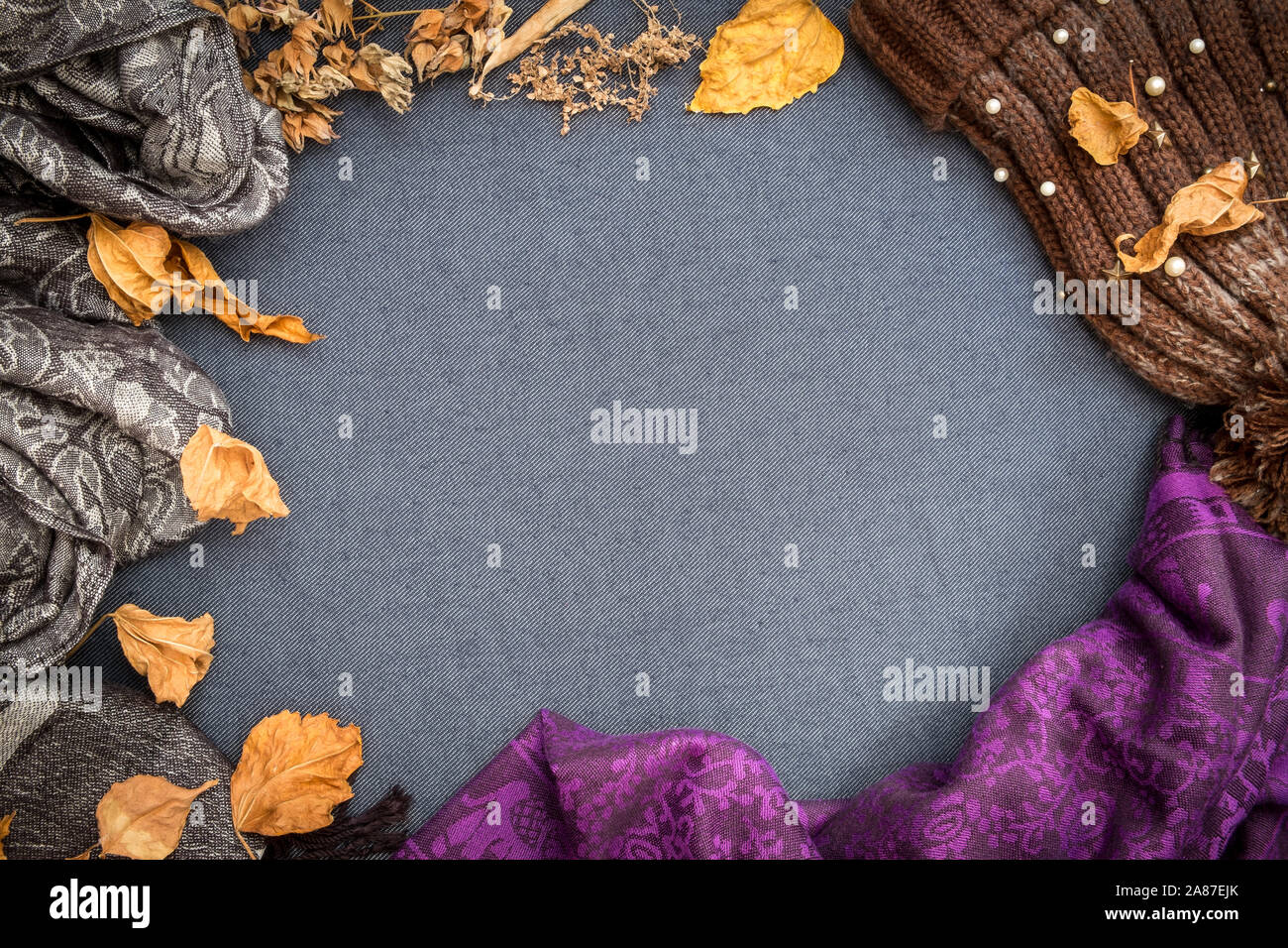 Automne hiver télévision lay. Bonnet tricoté marron, violet foulard et des feuilles sèches sur fond blanc bleu. Banque D'Images