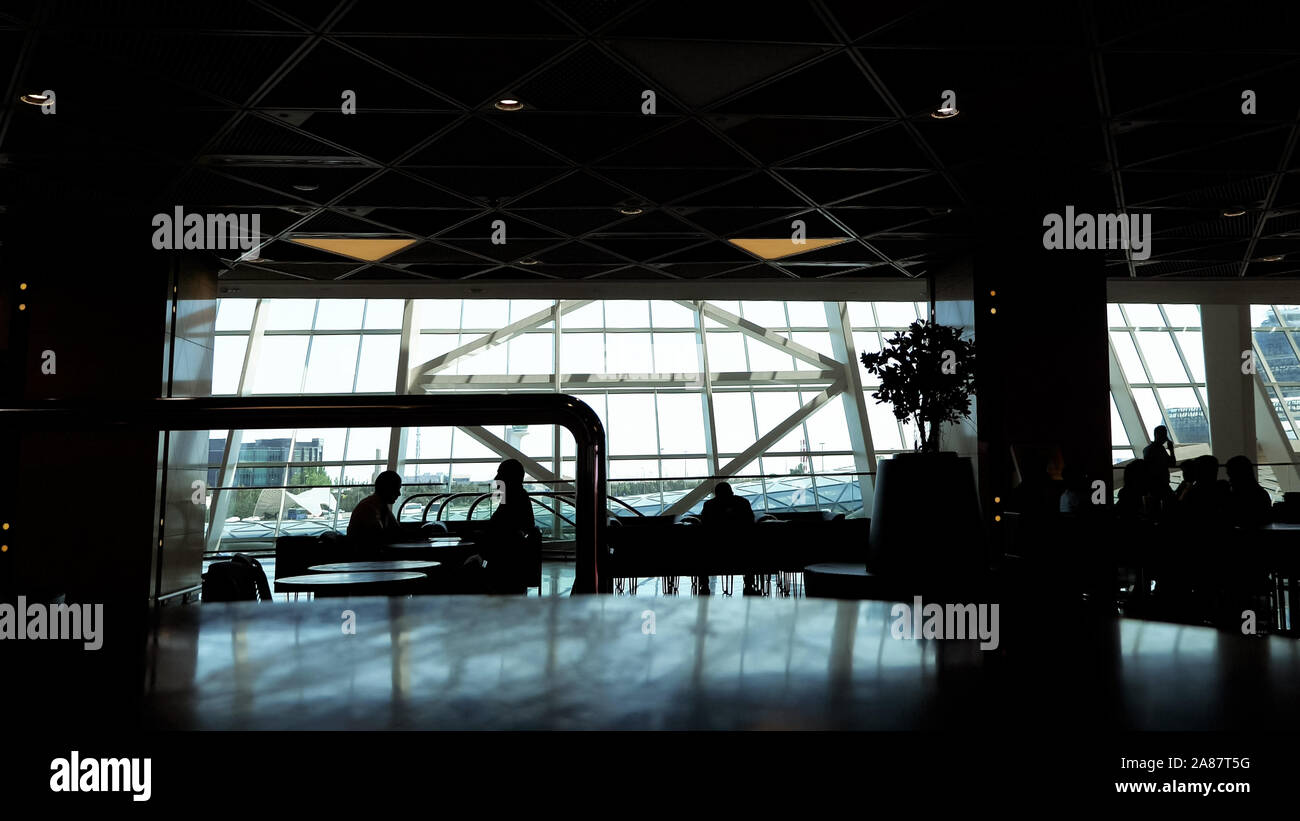 Les gens attendent leur vol dans l'aéroport. Silhouettes de personnes dans cafe à terminal de l'aéroport avec fenêtres panoramiques. Zone d'attente dans l'aéroport. Banque D'Images