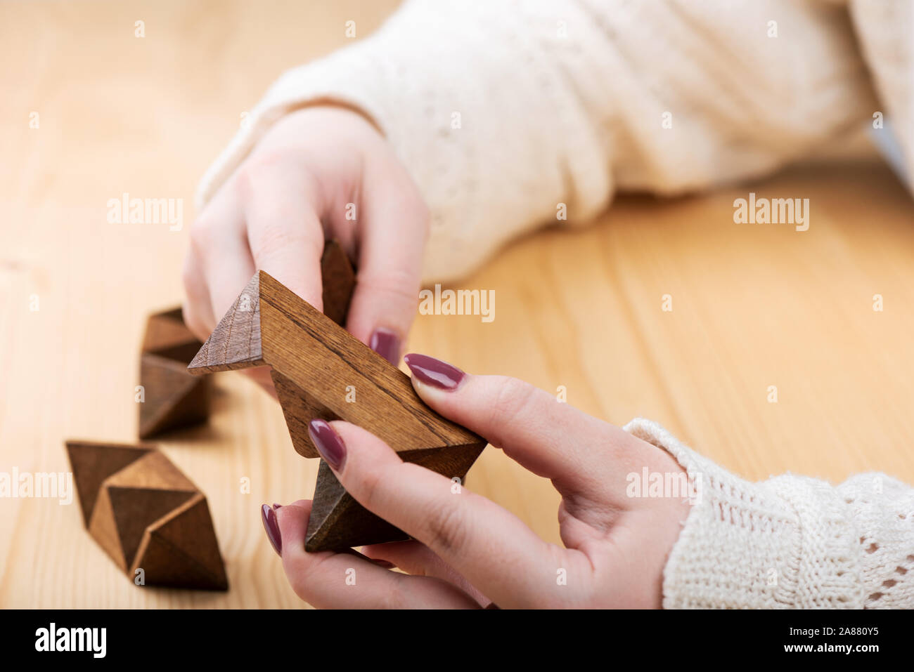 Une jeune fille tente d'assembler un puzzle dodécaèdre en forme d'étoile. Douze faces petit dodécaèdre en forme d'étoile sur une table en bois. Puzzle concept. Banque D'Images