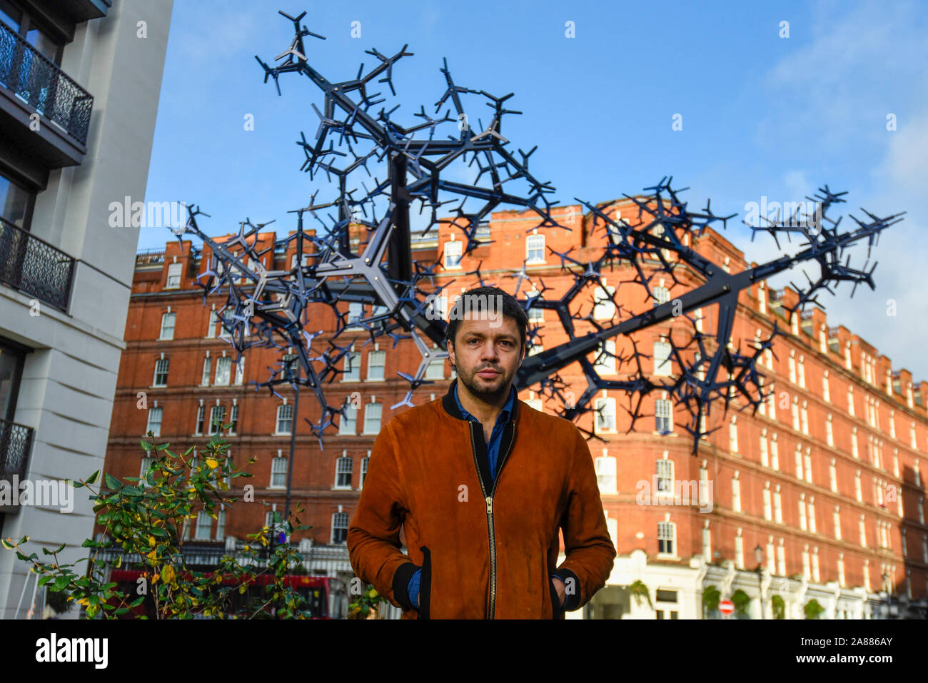 Londres, Royaume-Uni. 7 novembre 2019. Conrad Shawcross RA pose à côté de son nouveau travail' à 'régime bicaméral son dévoilement au Chelsea Barracks. Les 8m de hauteur sculpture est en aluminium anodisé formé de près de 700 composants et ressemblent à des systèmes naturels, y compris les voies nerveuses ou un arbre. schématisées C'est la première œuvre commandée pour Chelsea Barracks, quartier le plus récent. Crédit : Stephen Chung / Alamy Live News Banque D'Images