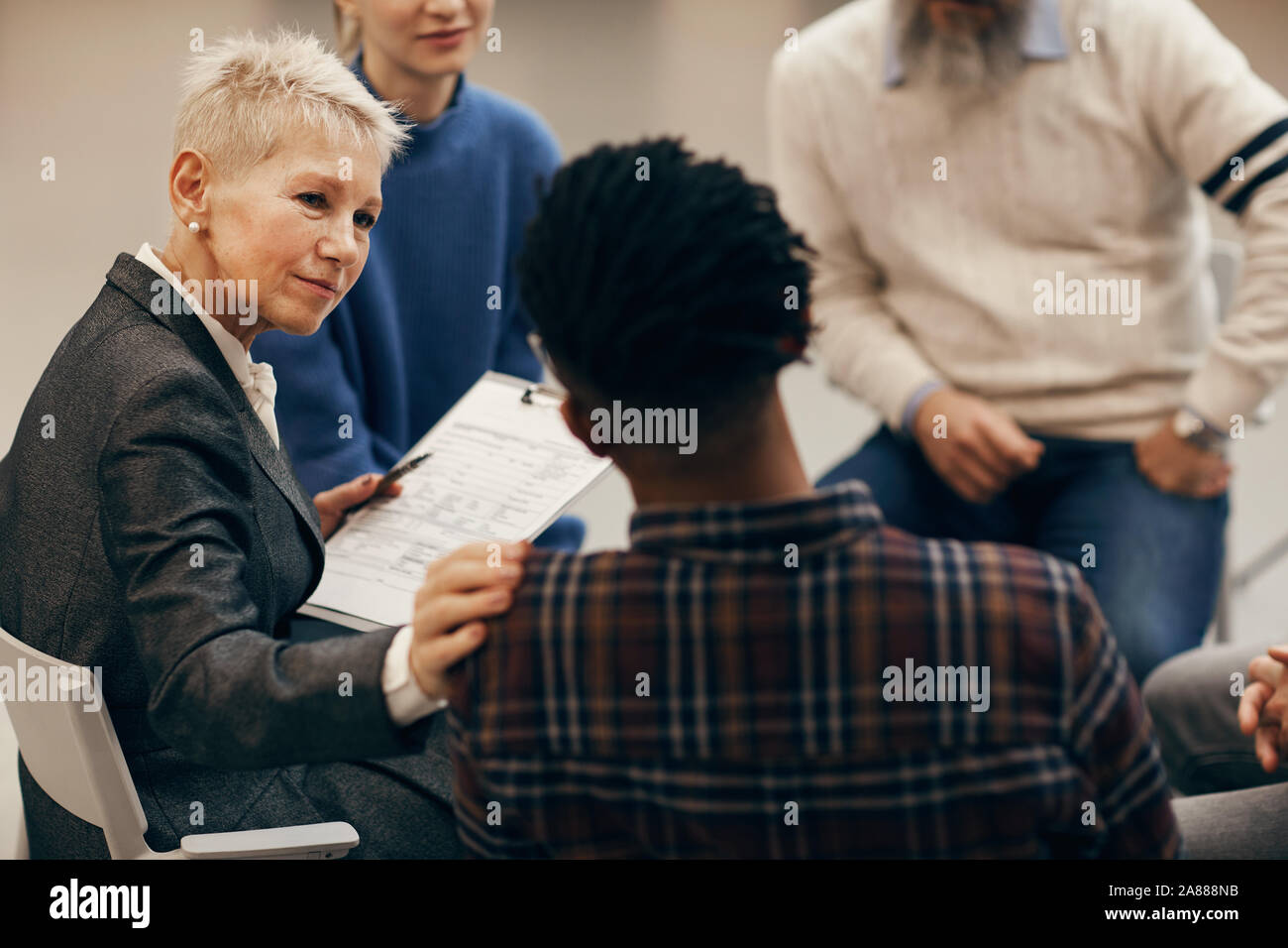 Femme mature avec de courts cheveux blonds à l'écoute des jeunes de l'Afrique de l'homme et le soutenir pendant le traitement avec la classe de leçon Banque D'Images