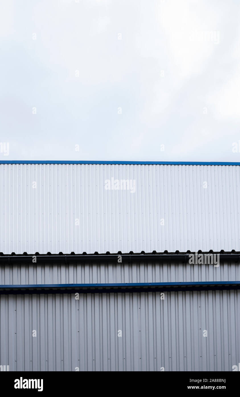 Plaques ondulées métalliques sur un bâtiment avec un bleu metal coins. Toit ondulé en aluminium blanc pour mur ou contre feuilles ciel nuageux sur l'arrière-plan Banque D'Images
