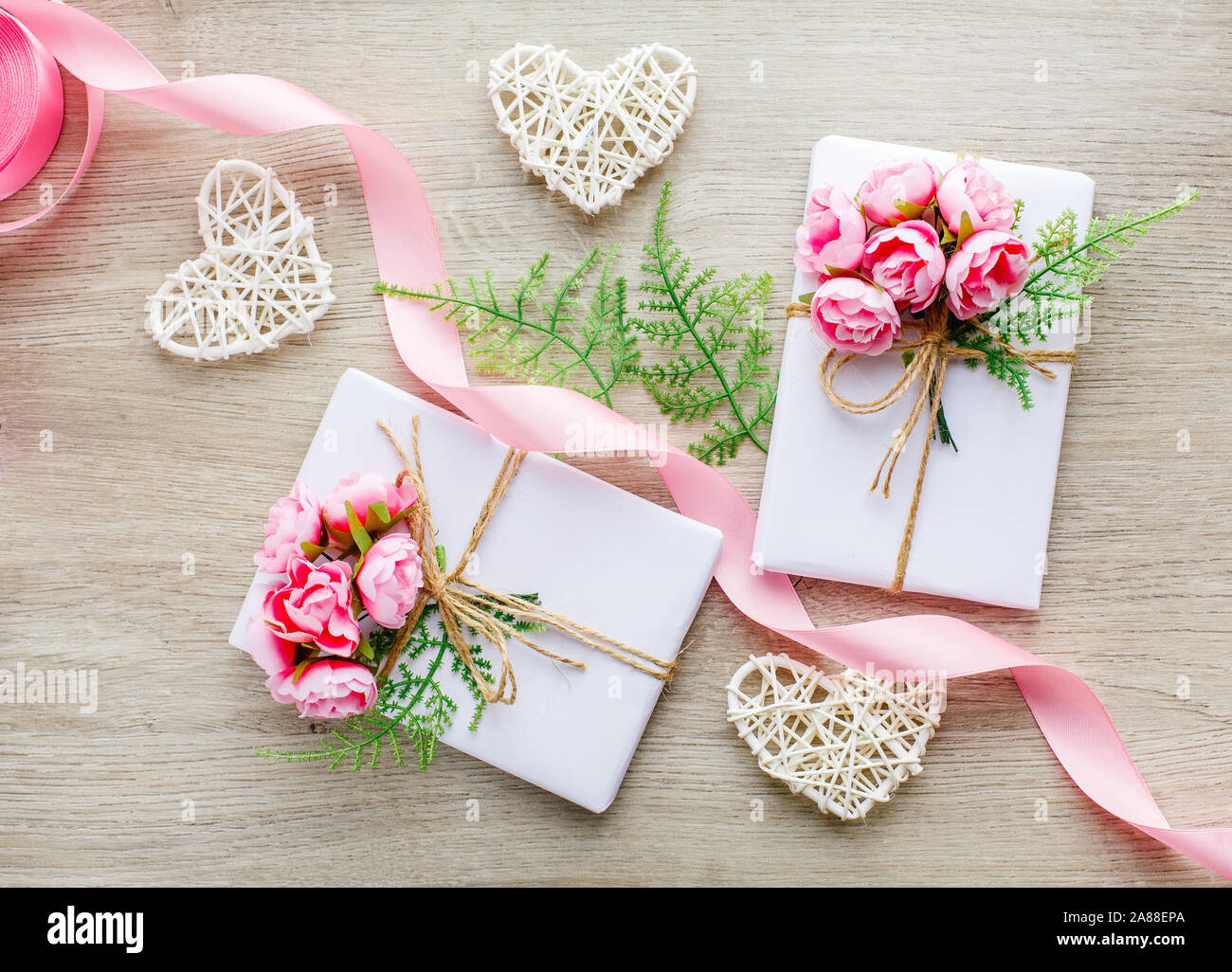 Composition avec boîtes cadeaux décorées de branche de grin, de roses, de coeurs en bois et de ruban rose satiné. Banque D'Images