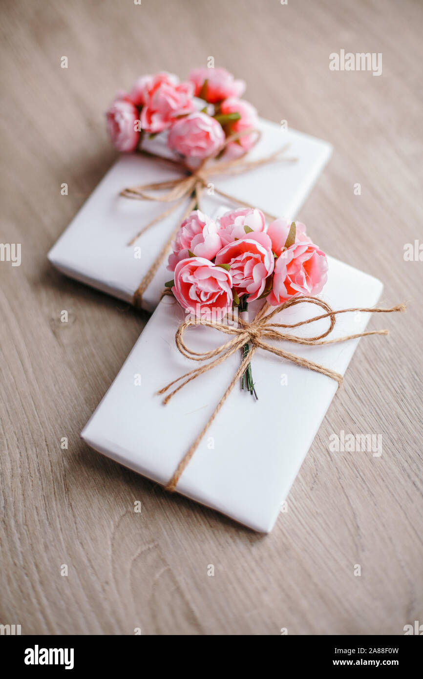 Quelques boîtes cadeau enveloppées de papier blanc artisanal simple et décorées avec un bouquet de roses et un bouquet d'eucalyptus. Banque D'Images
