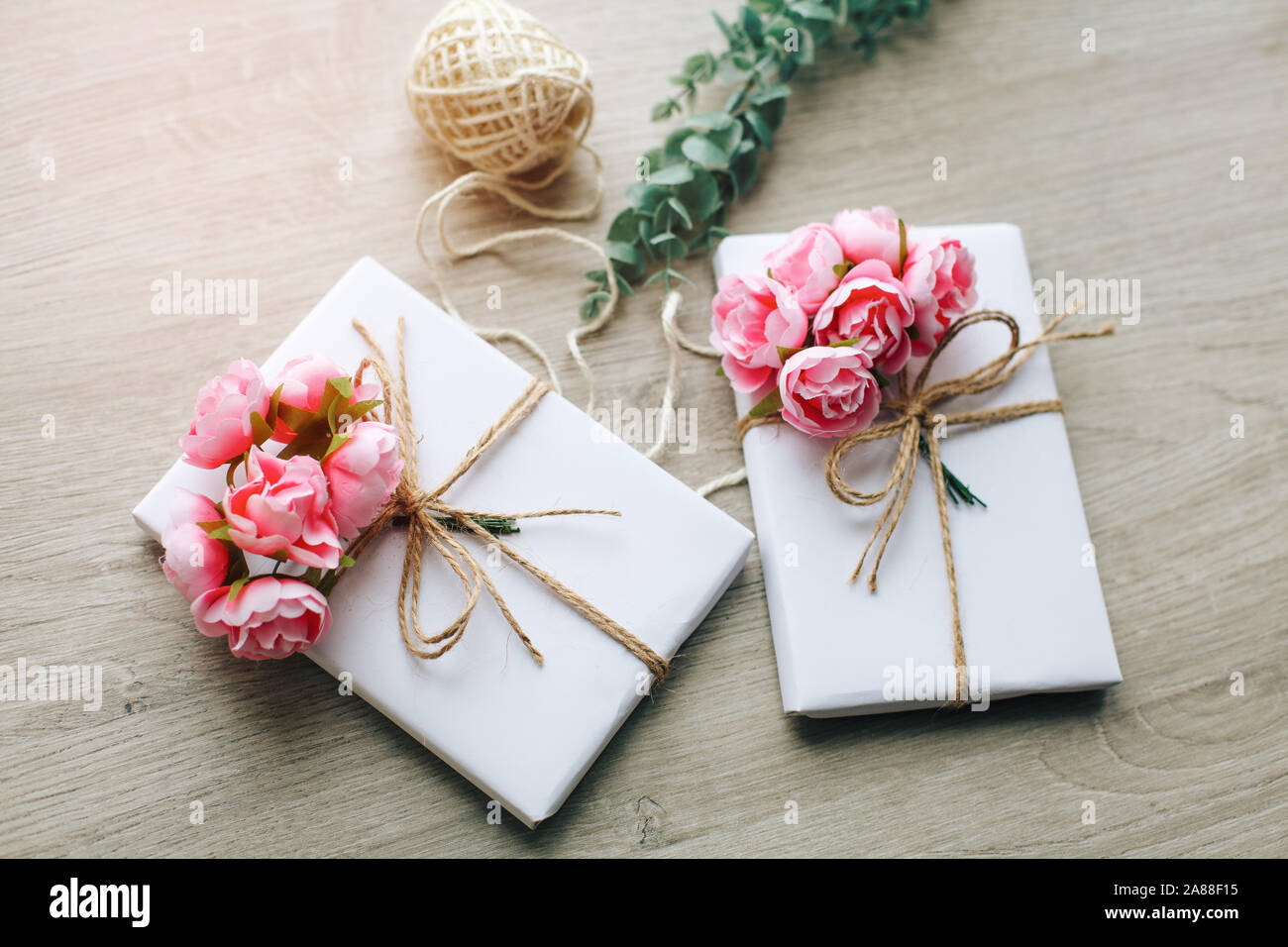 Boîte de cadeau faite à la main enveloppée de papier avec branche de roses. Branche d'eucalyptus et bobines rustiques de corde de chanvre sur fond Banque D'Images
