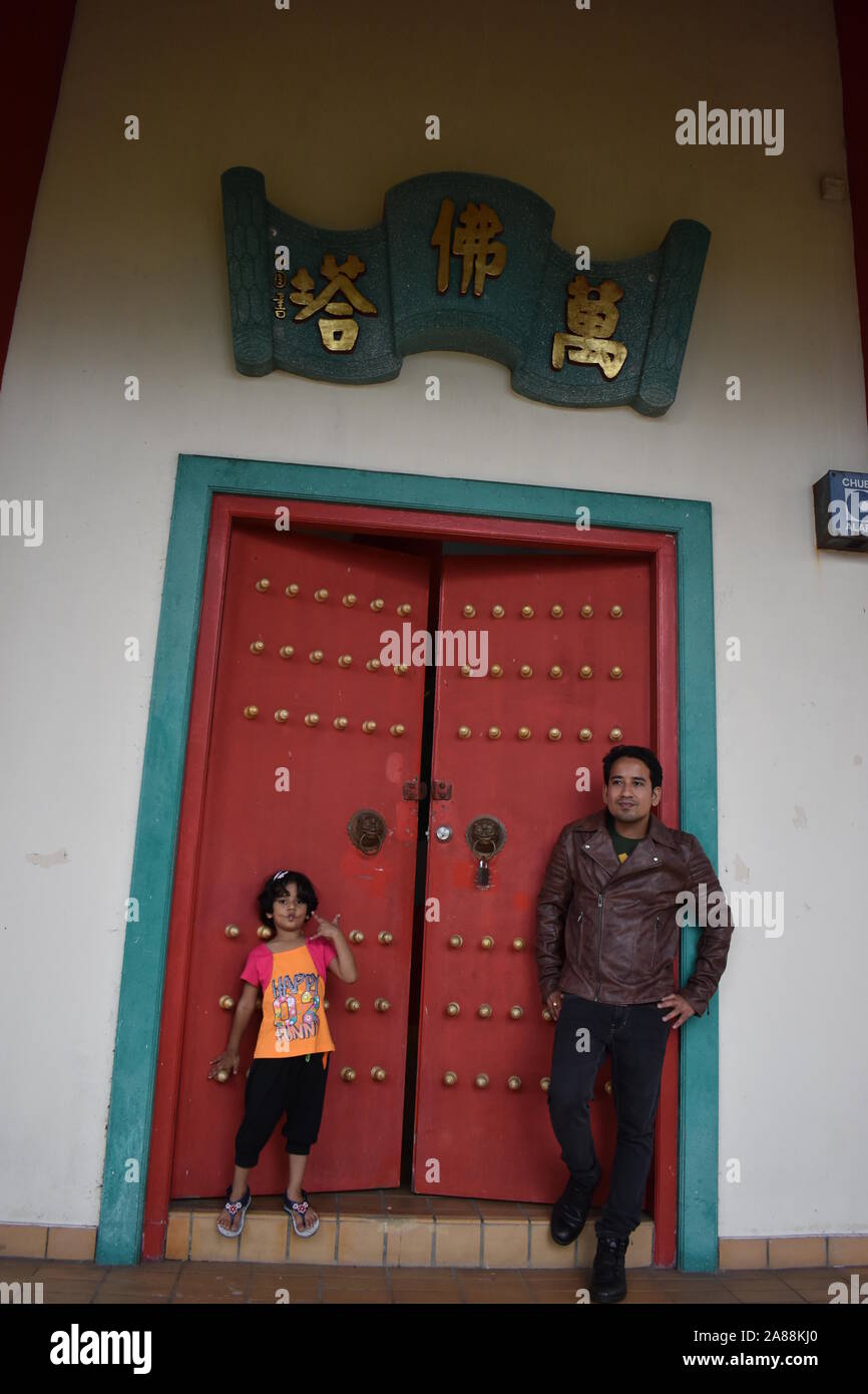 Un homme asiatique portant veste de cuir brun, avec sa fille debout devant brown porte artistique dans la région de Chin Swee temple, Cameron Highlands, Malaisie. Banque D'Images
