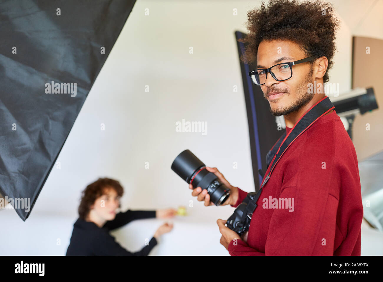 Le jeune photographe avec sa nouvelle optique d'appareil photo dans le studio photo Banque D'Images