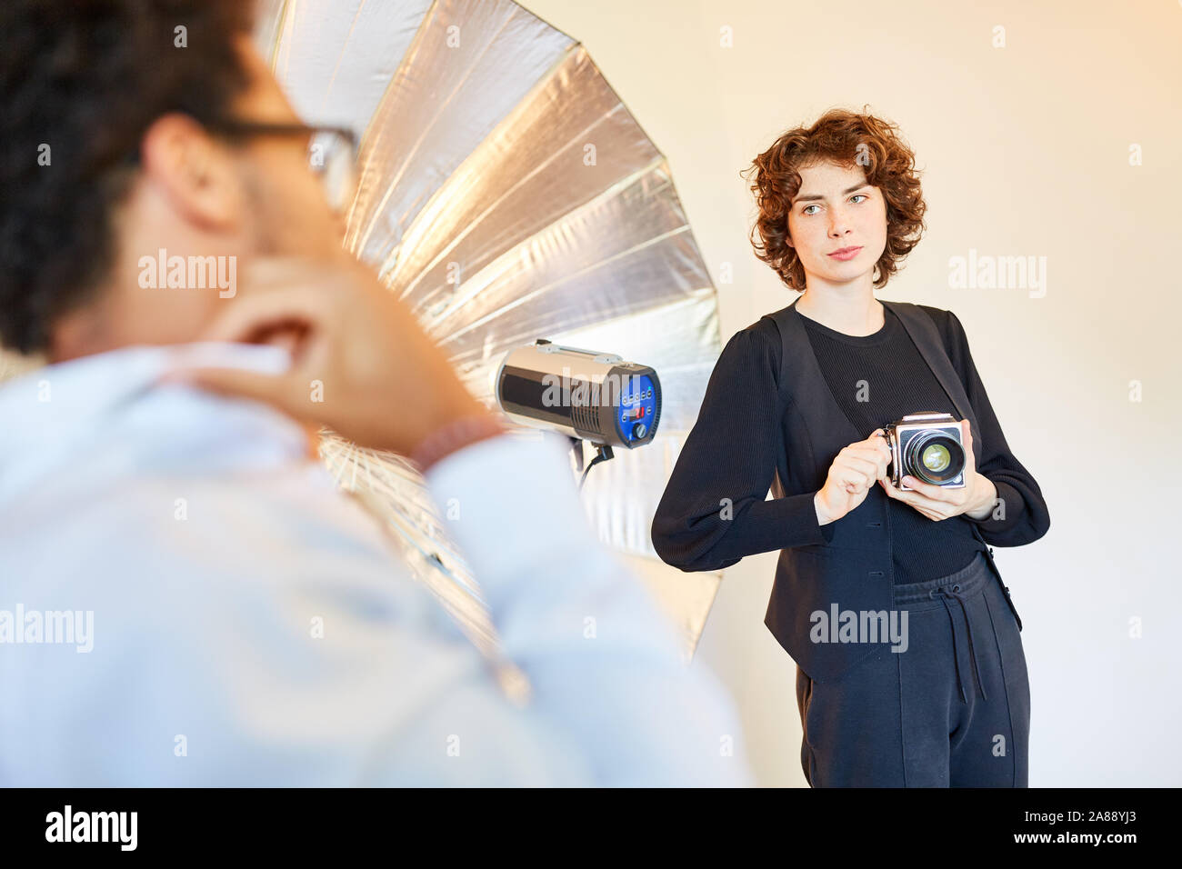 Le jeune photographe avec appareil photo prend des photos portrait d'un homme dans le studio Banque D'Images