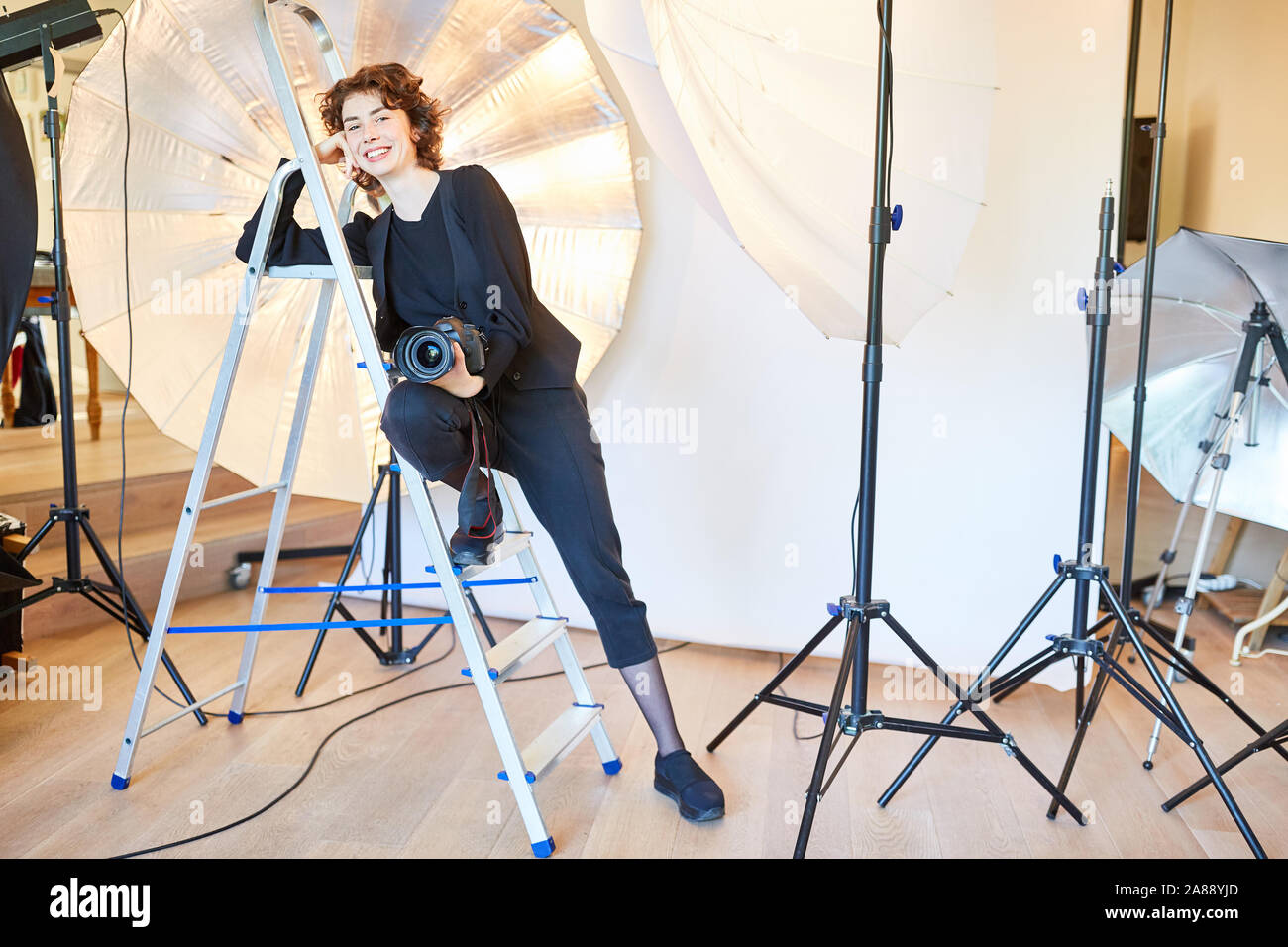 Photographe confiant avec l'appareil photo s'appuie contre une échelle dans le studio photo Banque D'Images