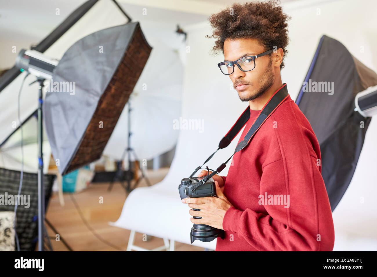 Jeune homme comme photographe pigiste avec appareil photo dans son studio photo Banque D'Images