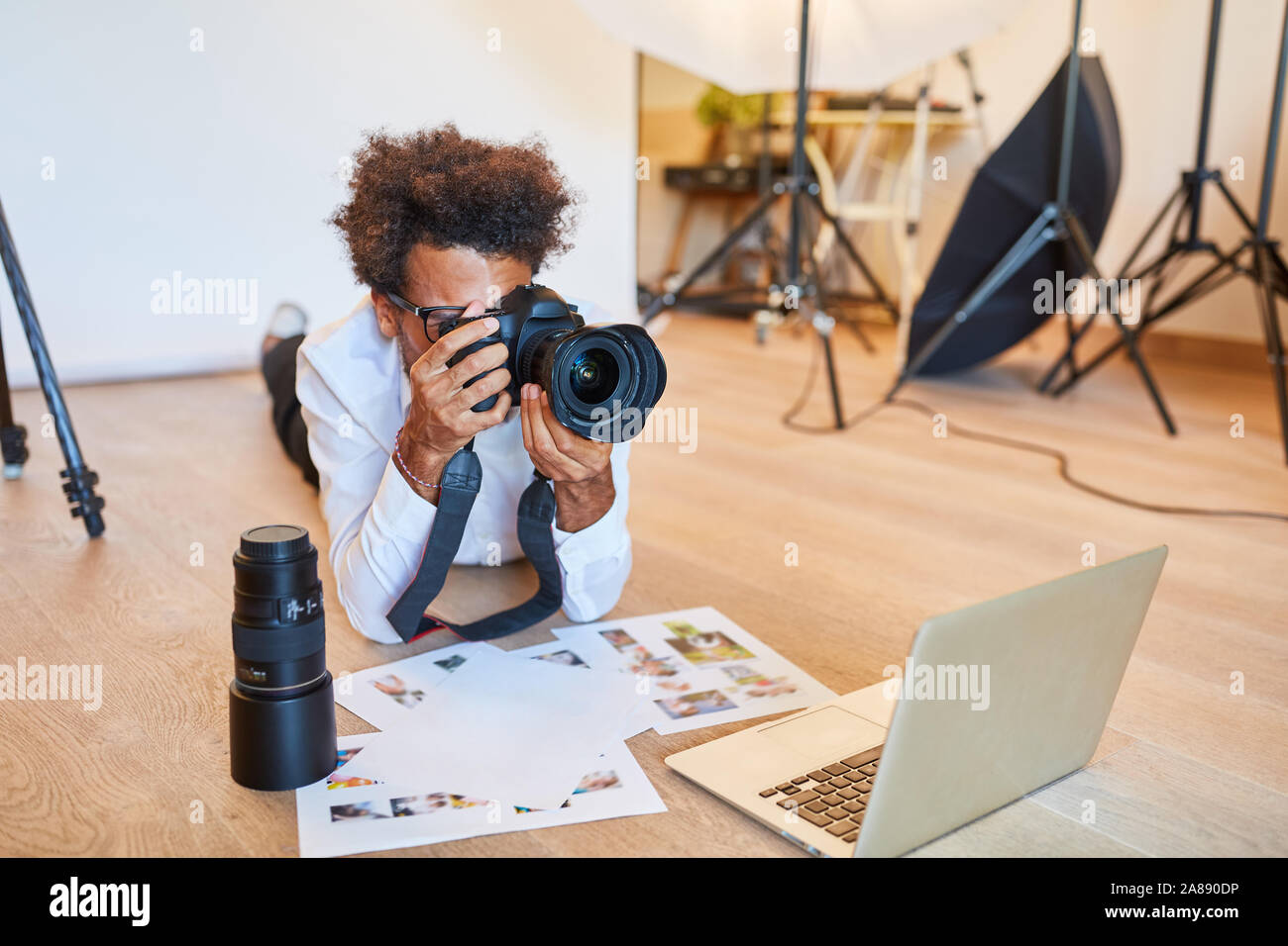 Le jeune photographe avec appareil photo et imprimer des photos dans le studio photo en face de l'ordinateur portable Banque D'Images