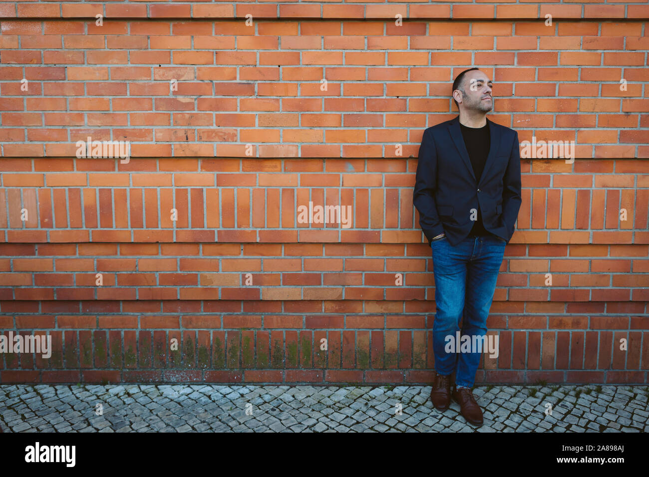 Homme portant un blazer et un Jean près d'un mur de briques Banque D'Images