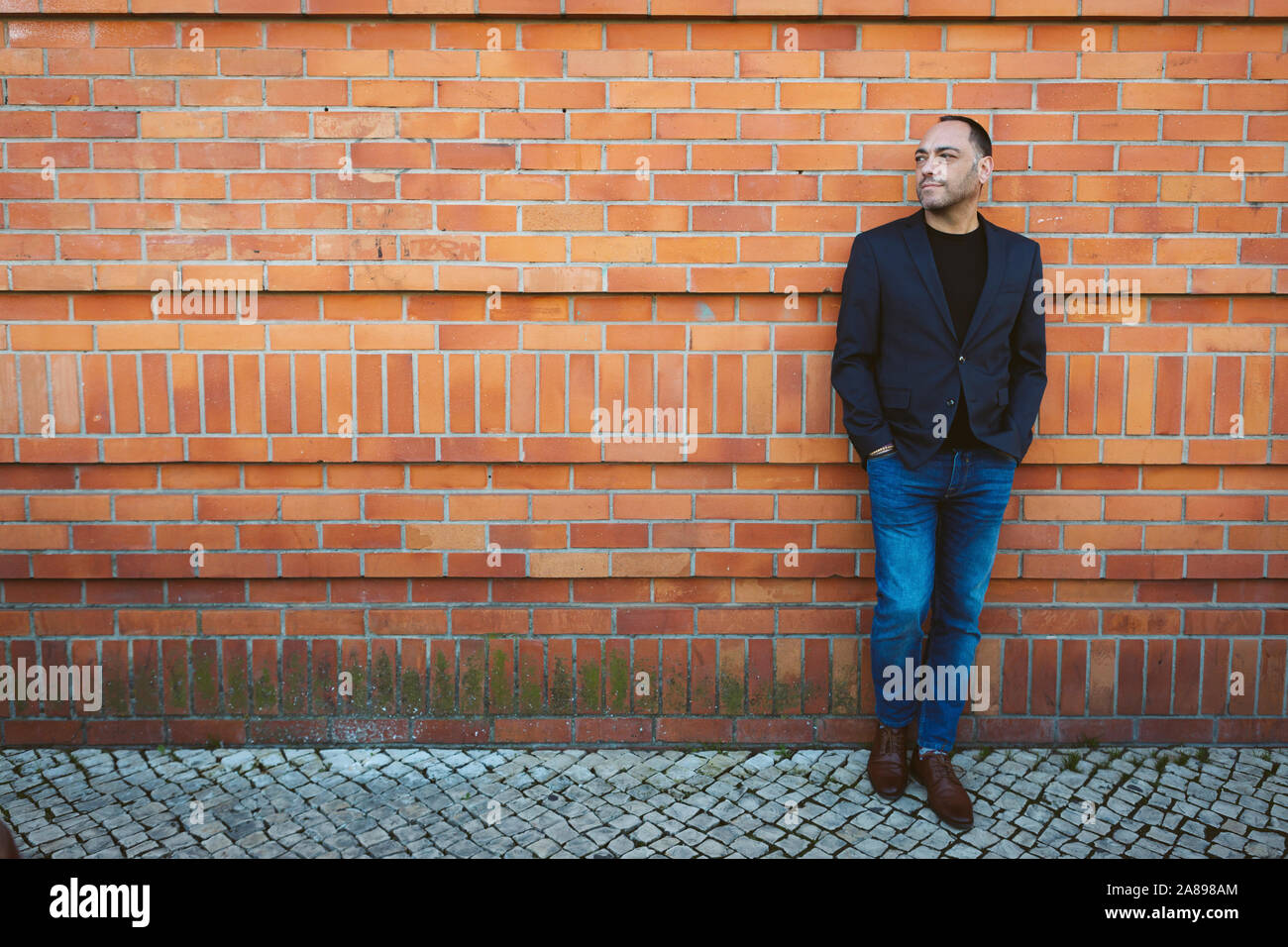 Homme portant un blazer et un Jean près d'un mur de briques Banque D'Images
