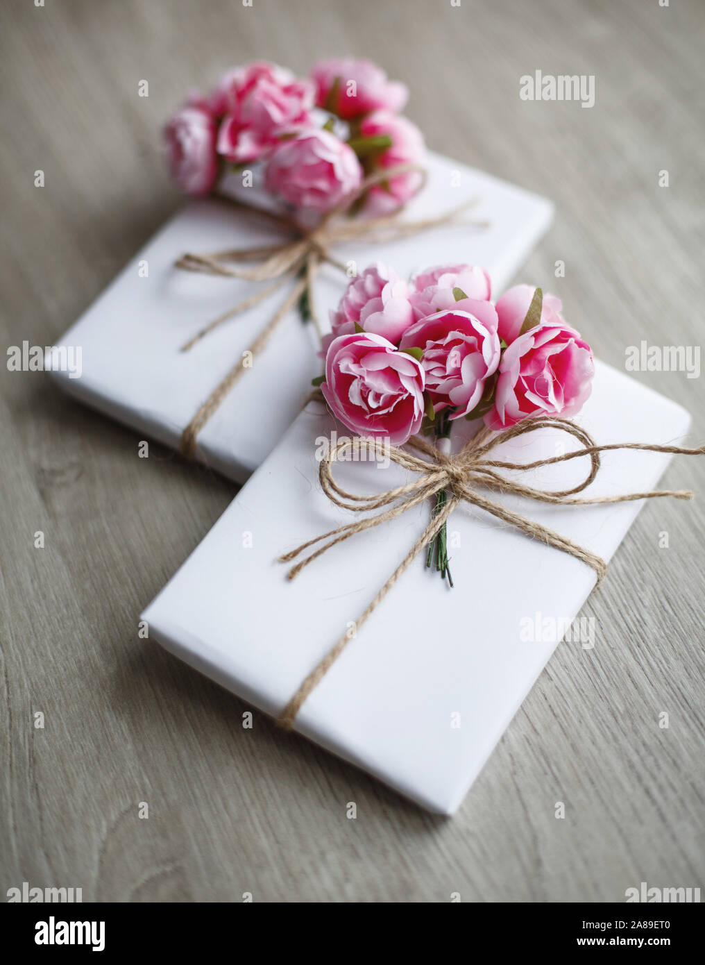 Boîte cadeau de style naturel fabriquée à la main sur une table en bois. Boîte cadeau faite à la main, enveloppée de papier blanc. Éléments de décoration à motifs floraux. Banque D'Images