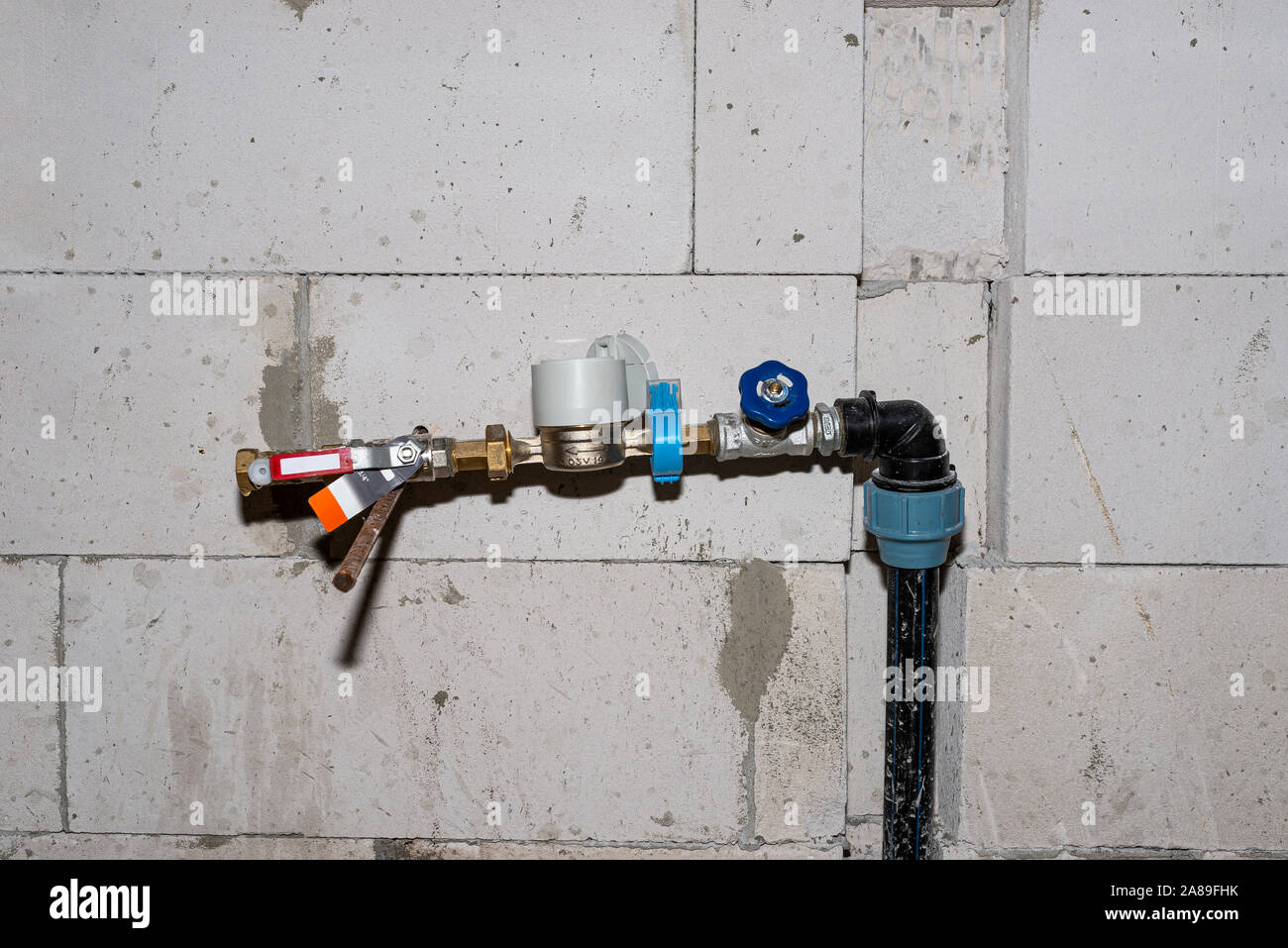 Une vanne d'eau temporaire avec un appareil connecté à un tuyau en PVC, installé dans une maison construite, contre le mur. Banque D'Images