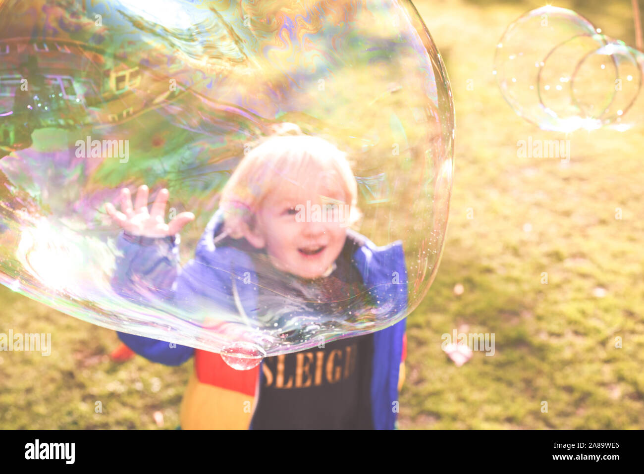 Enfant jouant à l'extérieur dans un jardin pendant la journée avec des bulles qu'il est heureux et en cours d'exécution Banque D'Images