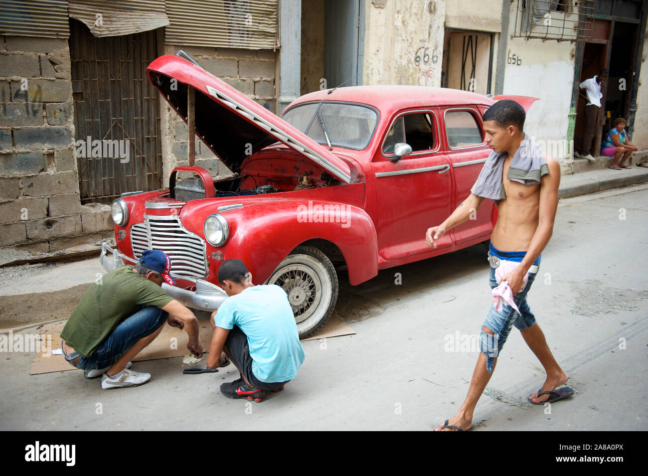 La Havane - 18 MAI 2011 : hommes cubains squat dans la rue à côté d'une voiture rouge vintage avec son capot entrouverte pour la réparation. Banque D'Images
