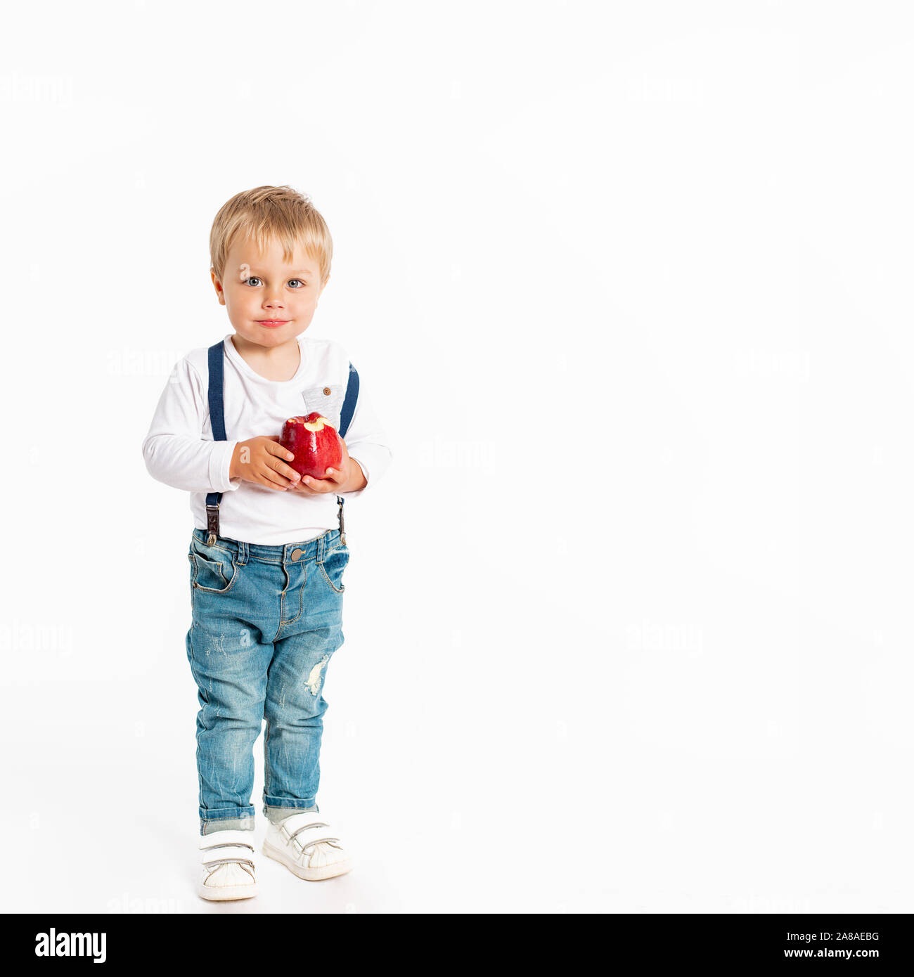 Baby Boy eating apple and smiling in studio isolé sur fond blanc. Concept d'aliments frais en bonne santé Banque D'Images