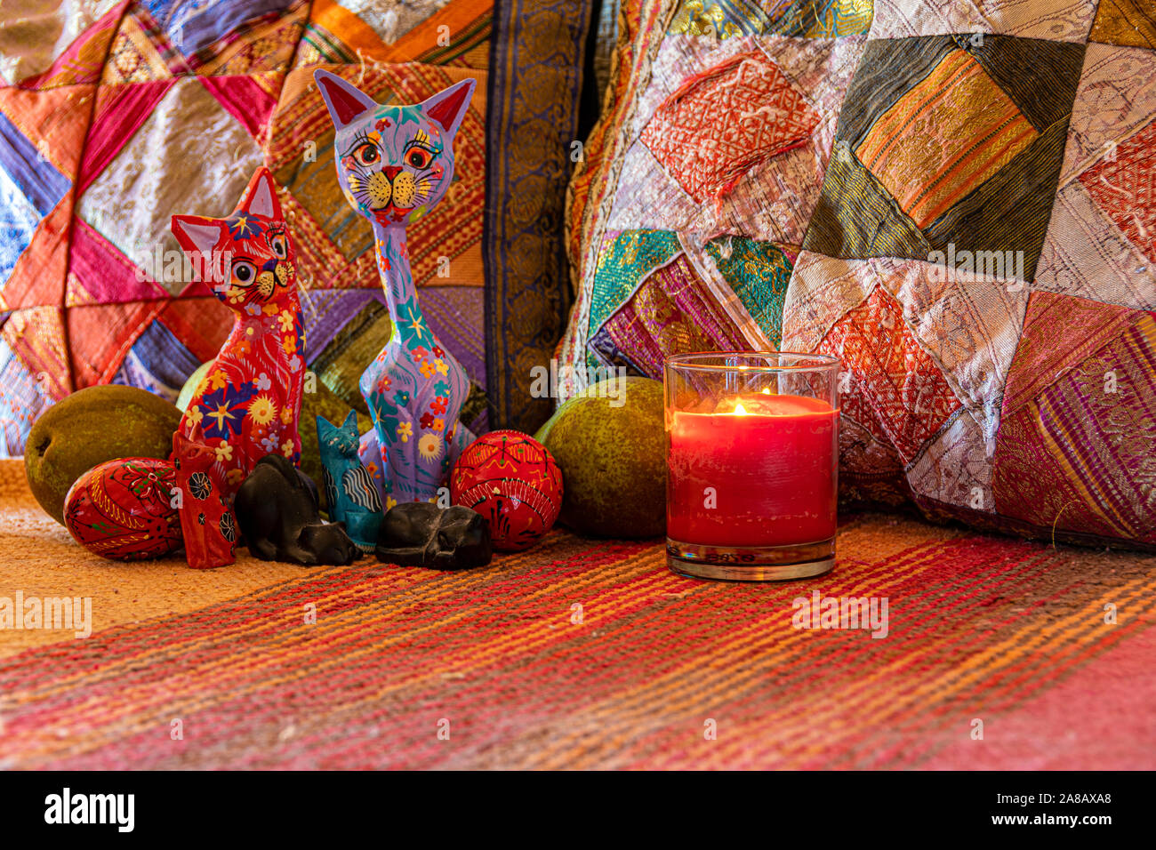 Composition décorative de chats multicolores entouré par les poires et les oeufs à la lumière d'une bougie et à l'arrière-plan de coussins multicolores. Banque D'Images