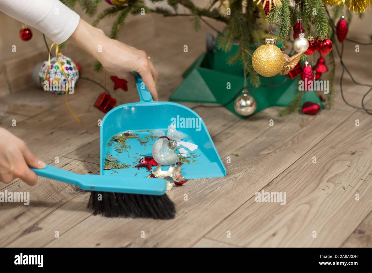 Les mains propres le cassé Boule de Noël à partir de la parole sous l'arbre de Noël. Femmes balayer le verre brisé de la boule de Noël. Banque D'Images