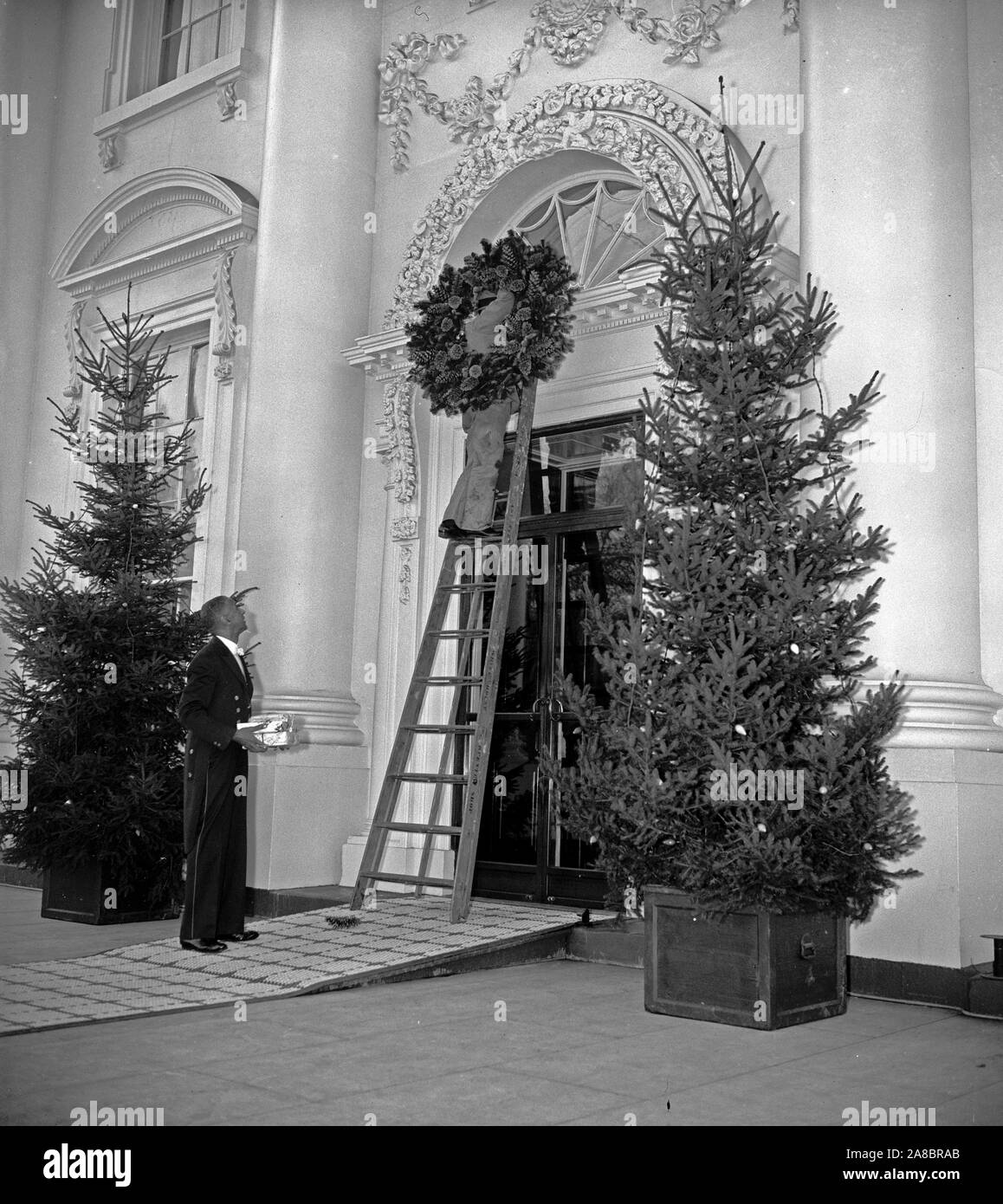 Esprit de Noël à l'air à la Maison Blanche. Washington D.C., 21 décembre. Ouvriers plaçant une couronne de Noël sur la porte à la Maison Blanche aujourd'hui. 12/21/1937 Banque D'Images