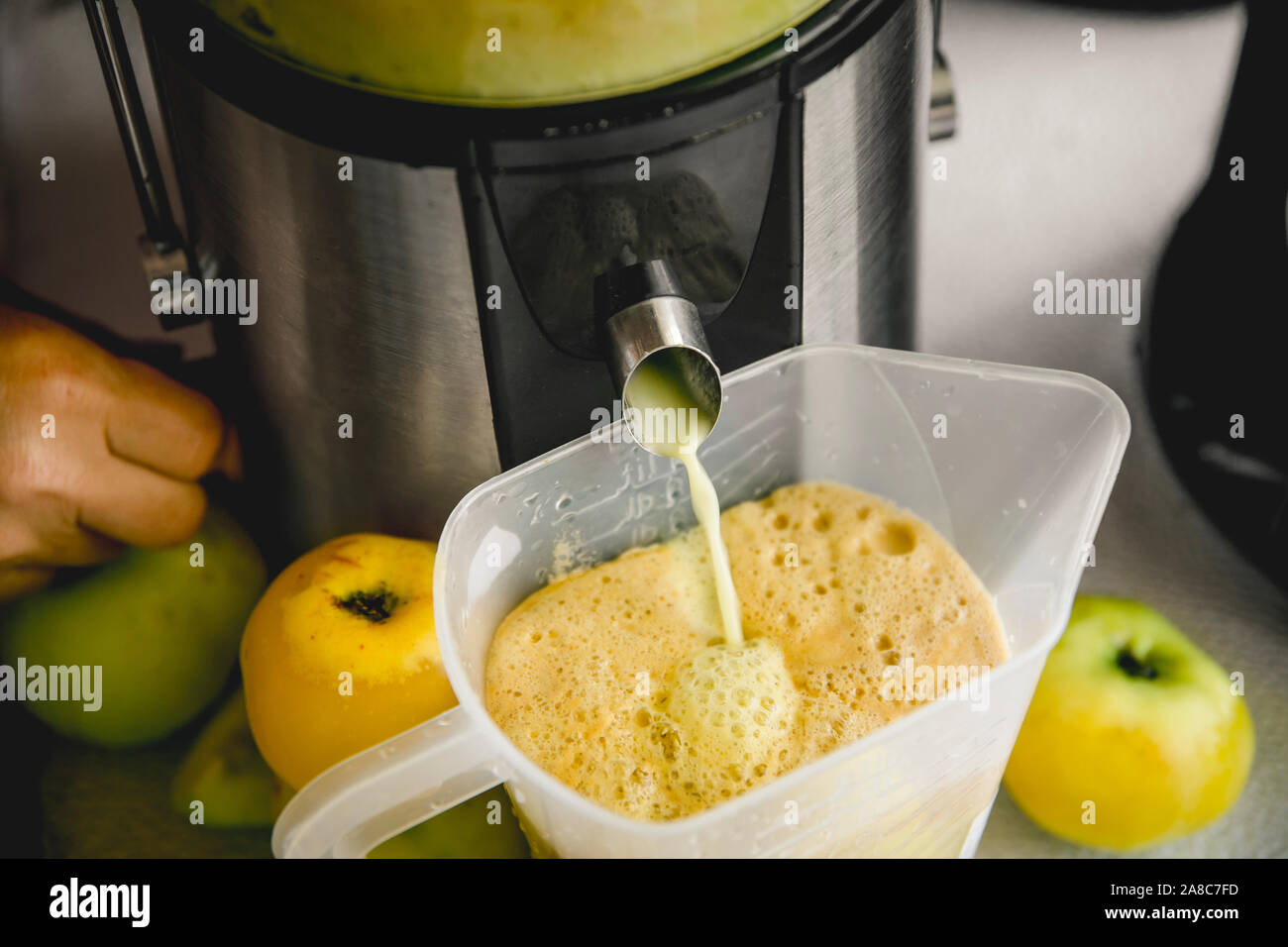 Faire du jus de pomme pressé frais à la maison en automne. Le jus frais traverse le tube de la machine dans une verseuse. Banque D'Images