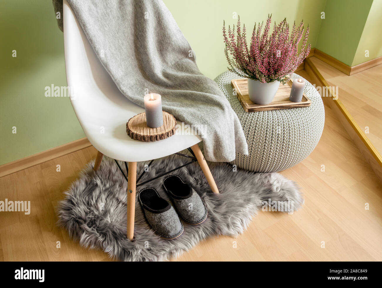 Chaise en plastique avec pieds en bois recouverts de plaid en laine grise, table en plastique tricoté, fausse couverture en peau de mouton avec pantoufles en feutre et bruyère en fleur Banque D'Images