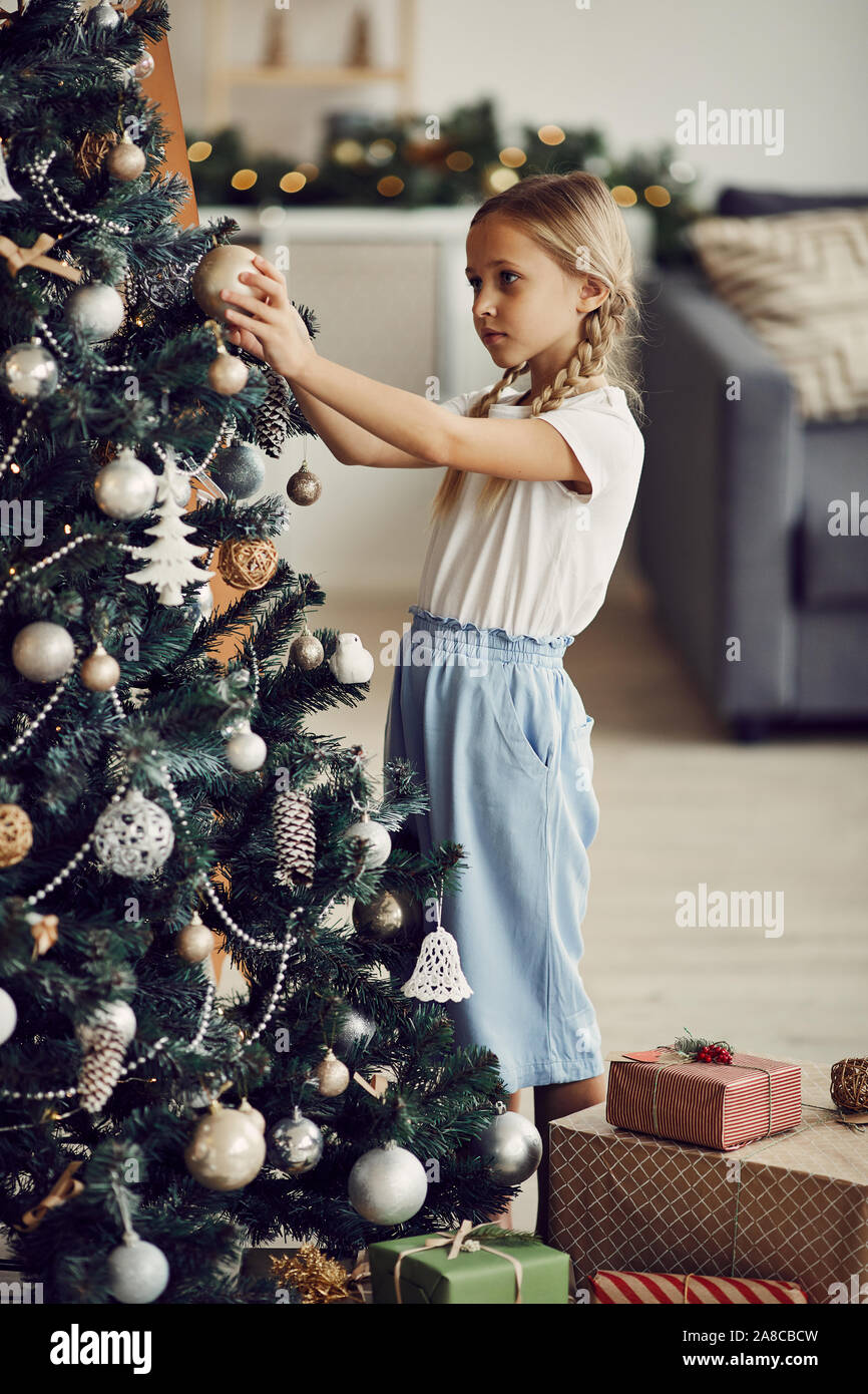 Petite fille aux cheveux blonds et permanent de l'arbre de Noël de décoration avec des jouets dans la salle de séjour à la maison Banque D'Images