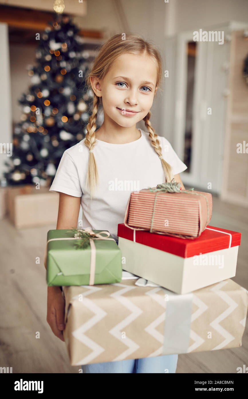 Portrait of little girl holding tas de cadeaux de Noël et à la caméra à tout en se tenant dans la chambre à la maison avec l'arbre de Noël Banque D'Images