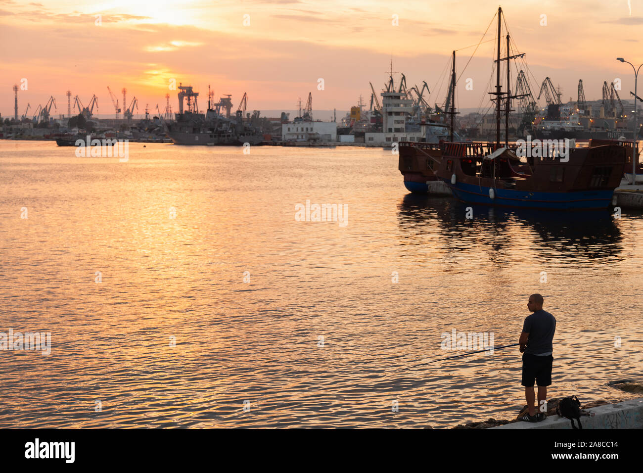 Varna, Bulgarie - 16 juillet 2014 : pêcheur se dresse sur un brise-lames dans le port de Varna au coucher du soleil Banque D'Images