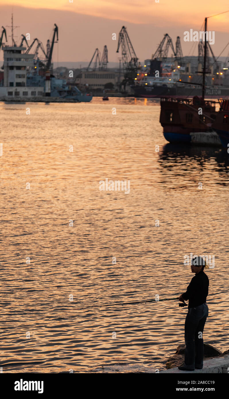 Varna, Bulgarie - 16 juillet 2014 : femme pêcheur se dresse sur un brise-lames dans le port de Varna au coucher du soleil. Photo verticale Banque D'Images