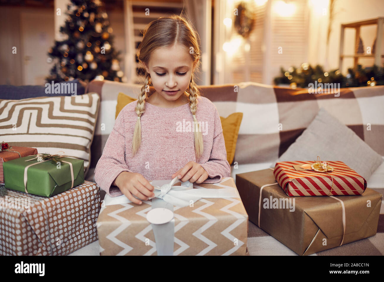 Petite fille assise sur le canapé et l'ouverture de gros cadeau de Noël qu'elle l'obtenant de Père Noël pour Noël à la maison Banque D'Images