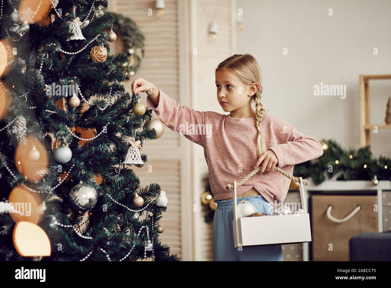 Petite fille aux cheveux blonds holding box avec des jouets dans ses mains et les accrocher sur l'arbre de Noël à la maison de vacances avant Banque D'Images