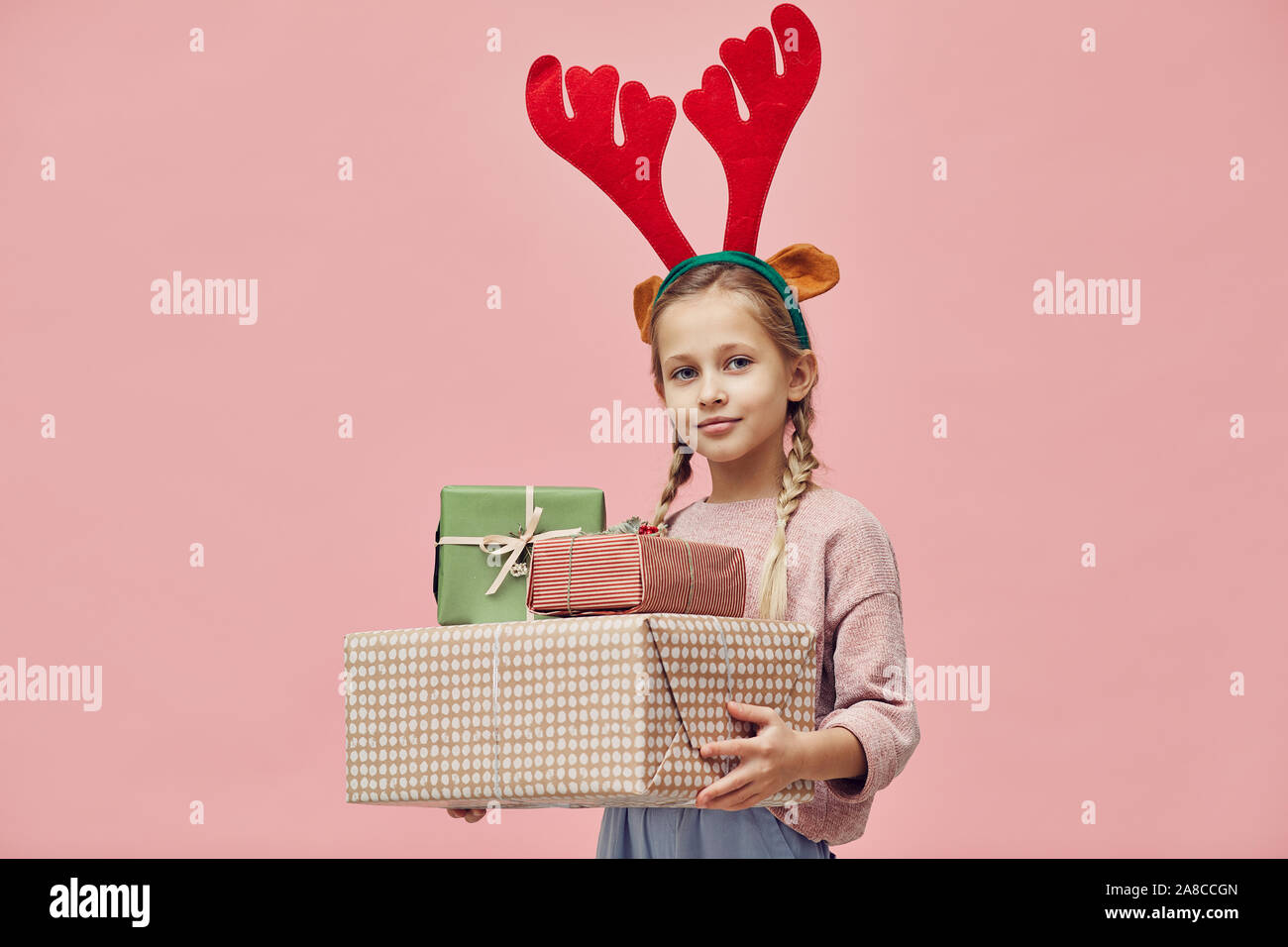 Portrait de petite fille en bois de cerf holding Christmas presents dans ses mains et smiling at camera isolé sur fond rose Banque D'Images