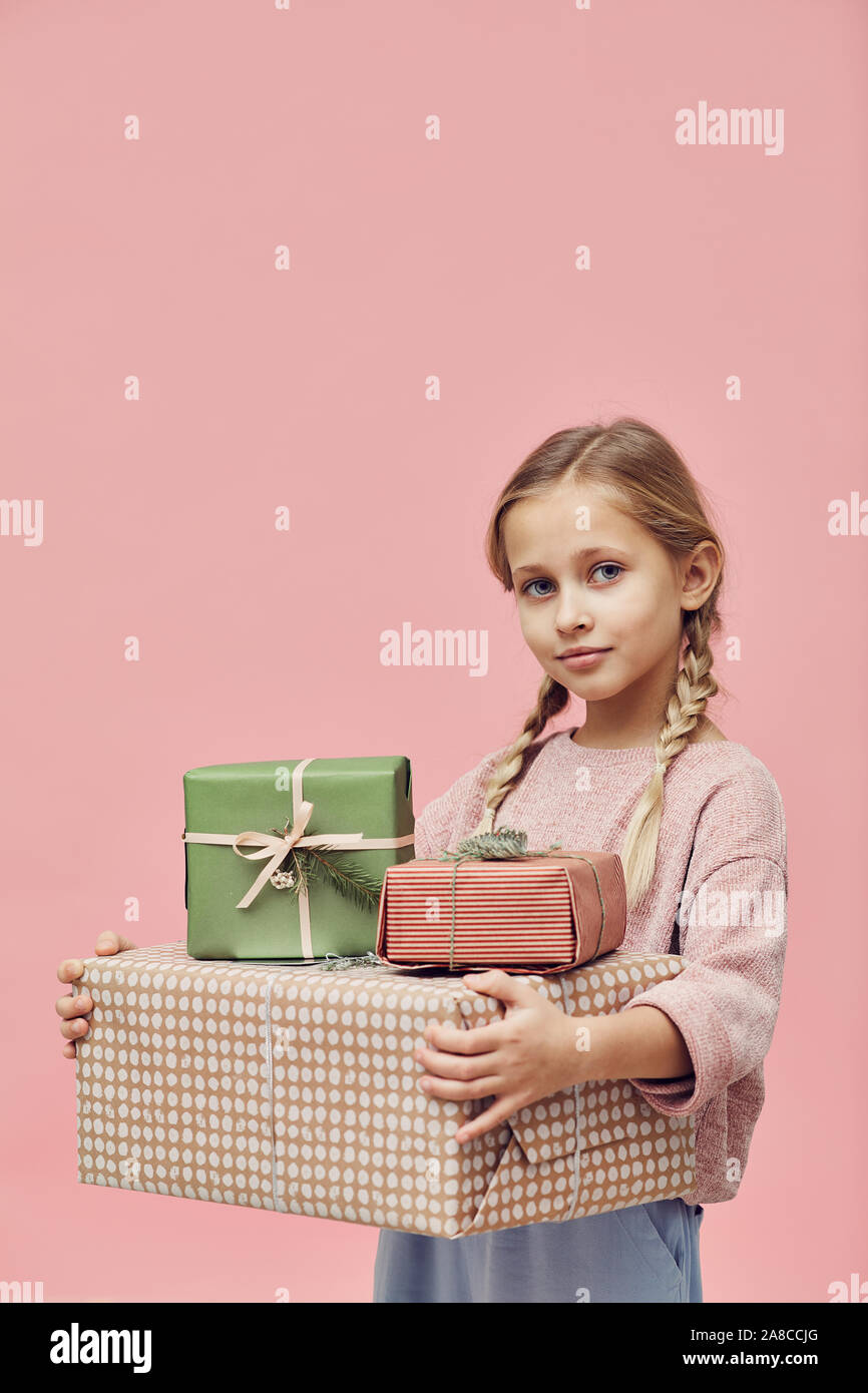Portrait of cute little girl holding wrapped gift boxes et à la caméra à l'encontre de la fond rose Banque D'Images