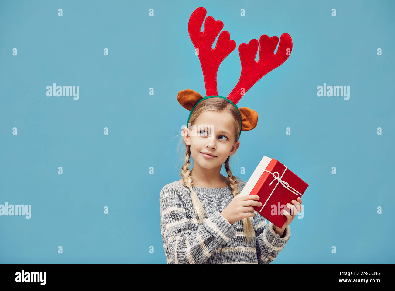 Petite fille en portant des bois de cerf rouge à poser avec caméra boîte cadeau rouge contre le fond bleu Banque D'Images