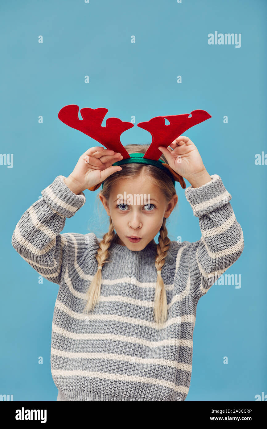 Portrait de funny little girl wearing bois de cerf et en prétendant le cerf de Noël contre le fond bleu Banque D'Images