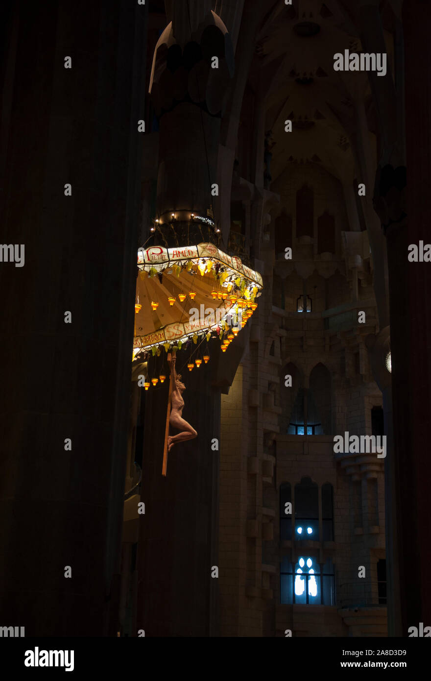 Sagrada Familia - intérieur. Lustre suspendu de Jésus parmi les sculptures hautes colonnes sur fond de vitraux de couleurs chaudes. Banque D'Images