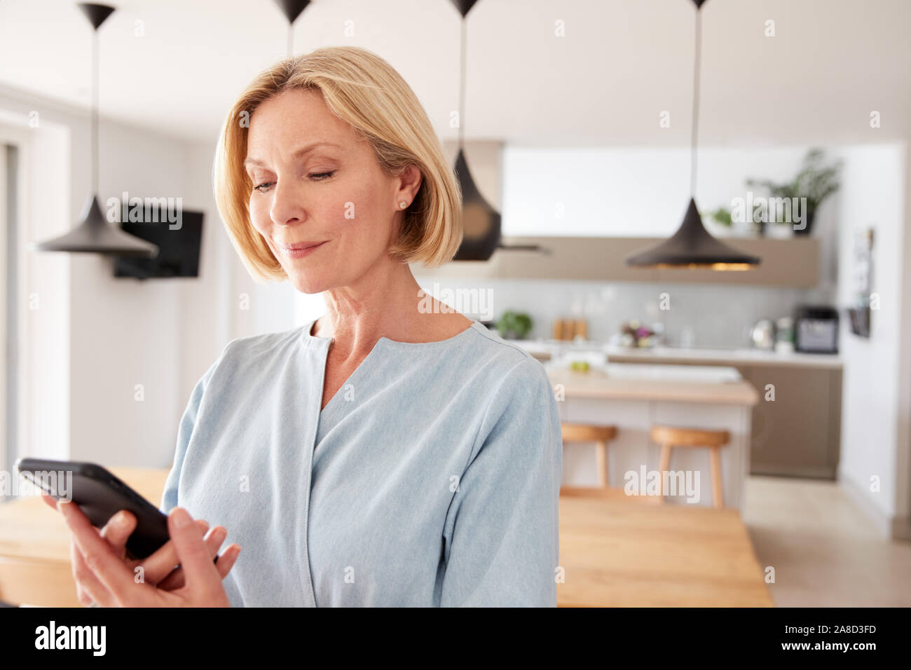 Femme mature à l'aide de l'App sur téléphone mobile pour contrôler la température du chauffage central dans la maison Banque D'Images