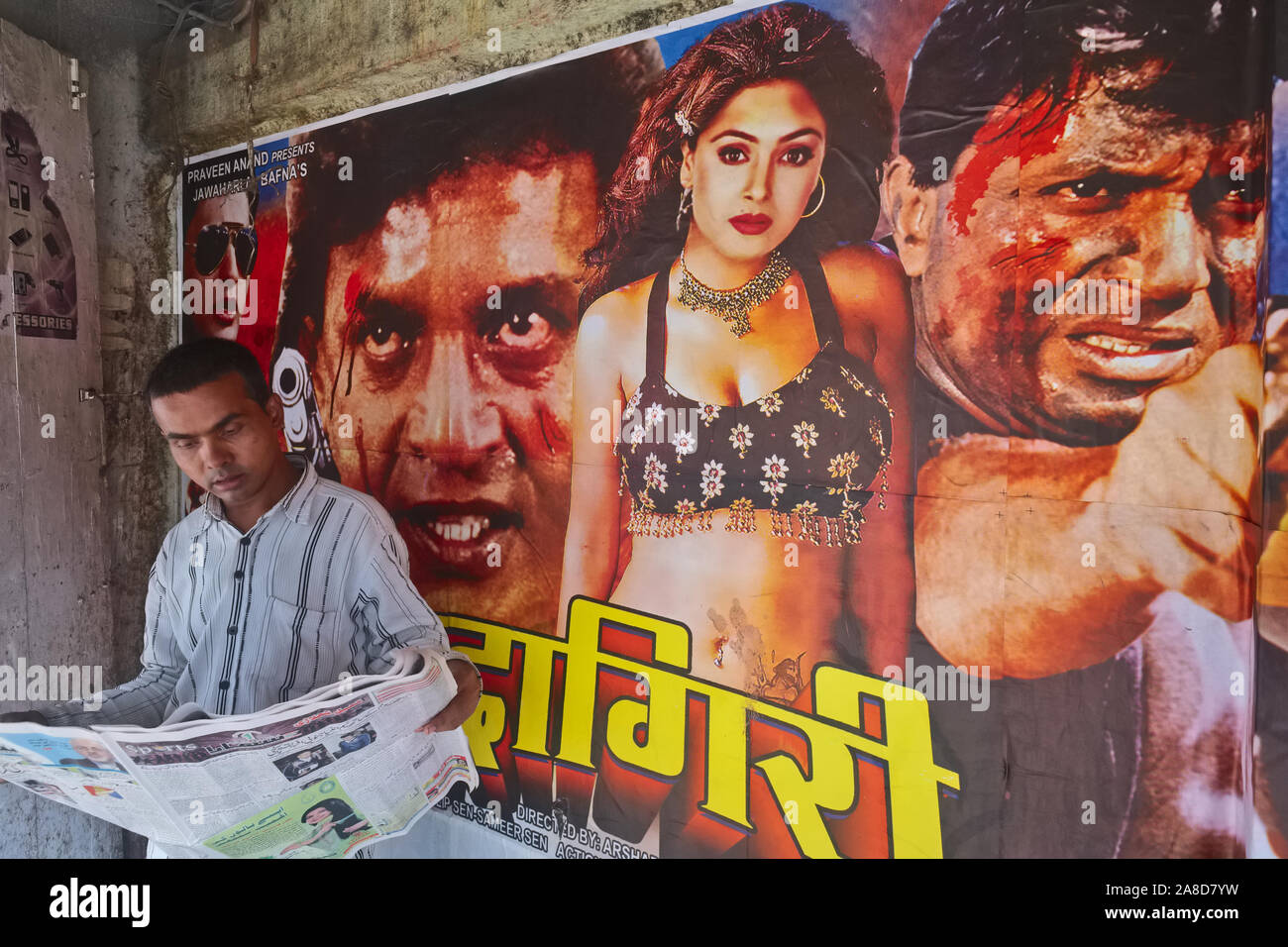 Un homme lit un journal devant une classe de travail bon marché l'industrie du cinéma dans la région de Grant Road de Mumbai, en Inde, le cinéma spécialisé dans les films hindi âgés Banque D'Images