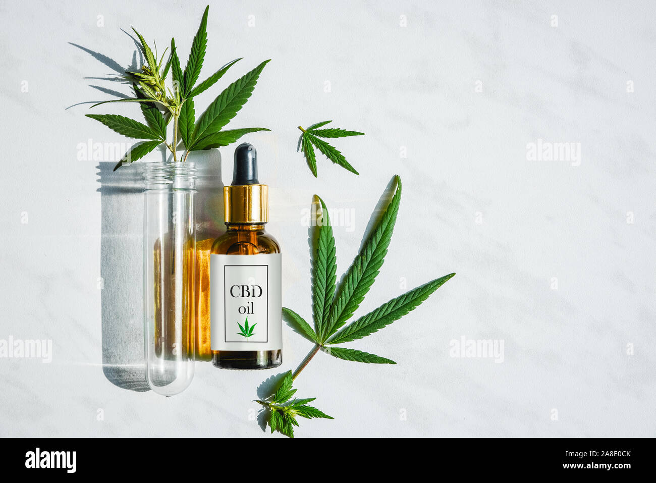 Le flacon en verre avec de l'huile de cannabis avec une étiquette et un tube à essai avec des feuilles de chanvre sur un fond de marbre Banque D'Images