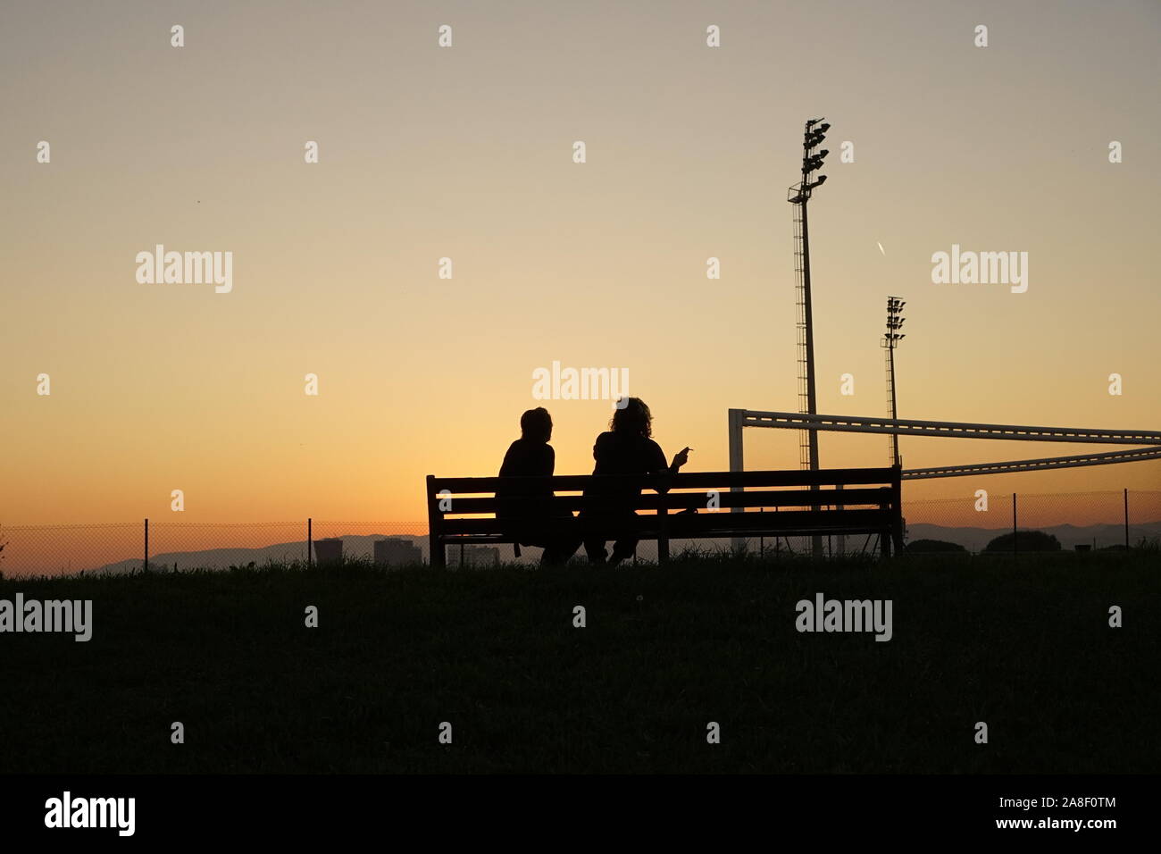 Un couple assis sur un banc dans le coucher du soleil au bord de la ville de Barcelone Banque D'Images