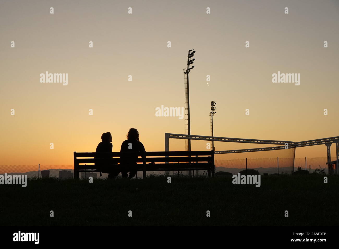 Un couple assis sur un banc dans le coucher du soleil au bord de la ville de Barcelone Banque D'Images