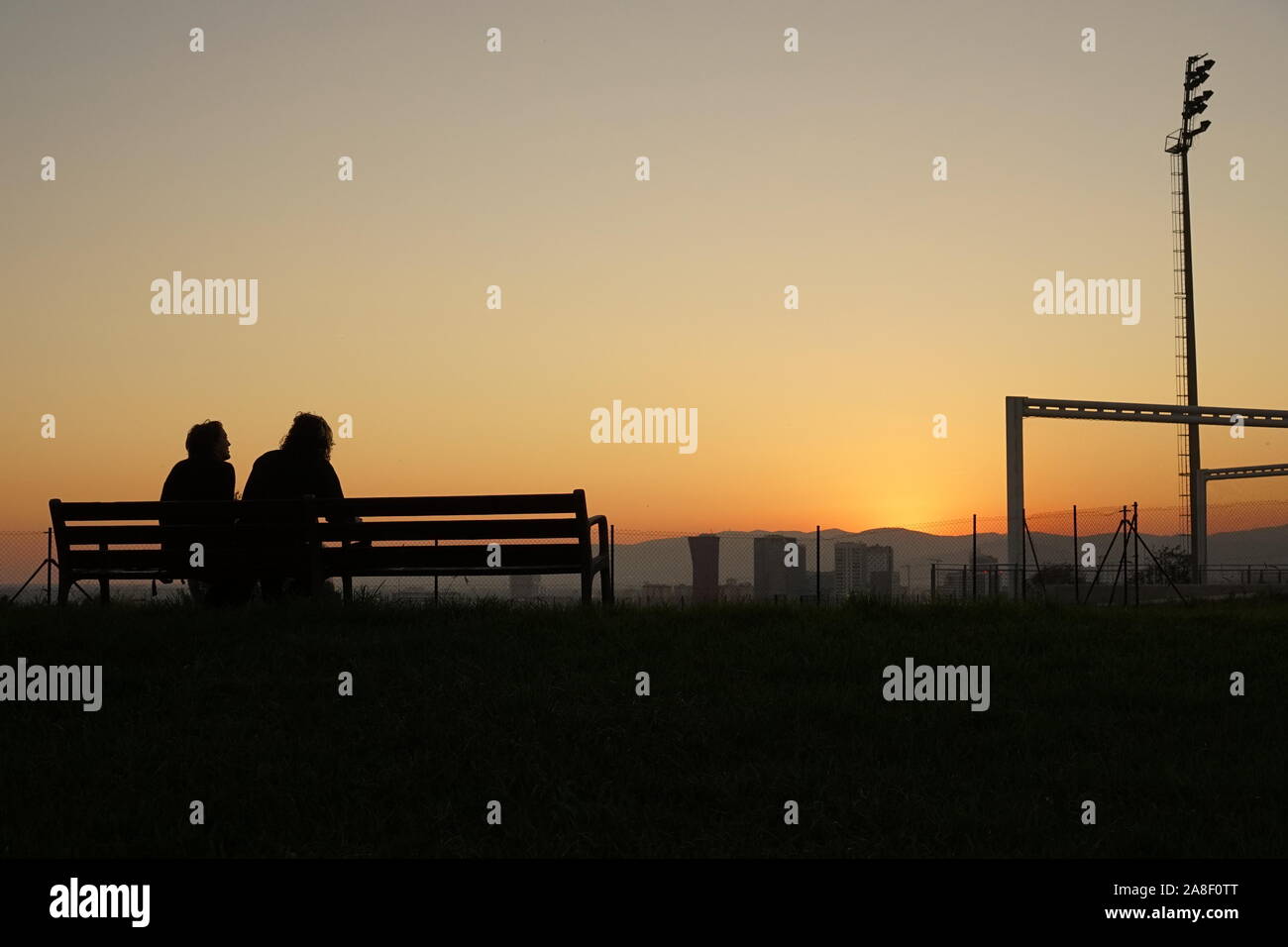 Un couple assis sur un banc dans le coucher du soleil au bord de la ville de Barcelone Banque D'Images
