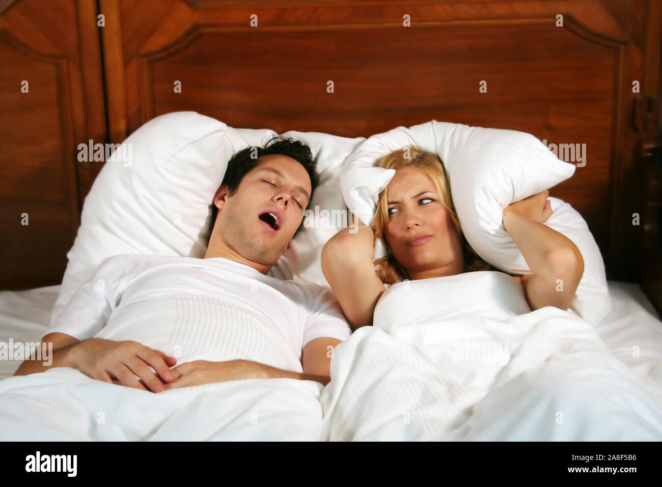 Mann schnarcht im Bett, Frau hält sich mit dem Kopfkissen die Ohren zu, M. : Oui Banque D'Images