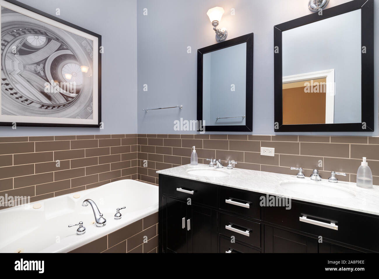 Un mur de la salle de bain bleu avec carreaux métro brun entourant la salle de bain, un meuble-lavabo de couleur sombre, et une photo sur le dessus de la baignoire. Banque D'Images