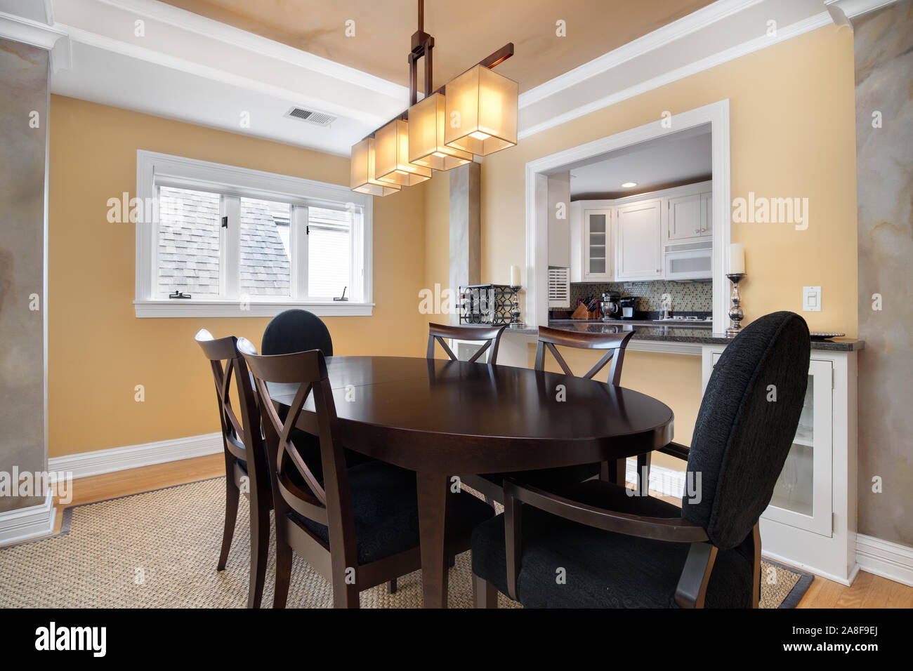 Une petite salle à manger dans un condo qui est dominé par une fenêtre de la cuisine. Une table et des chaises est centré sous un éclairage moderne. Banque D'Images